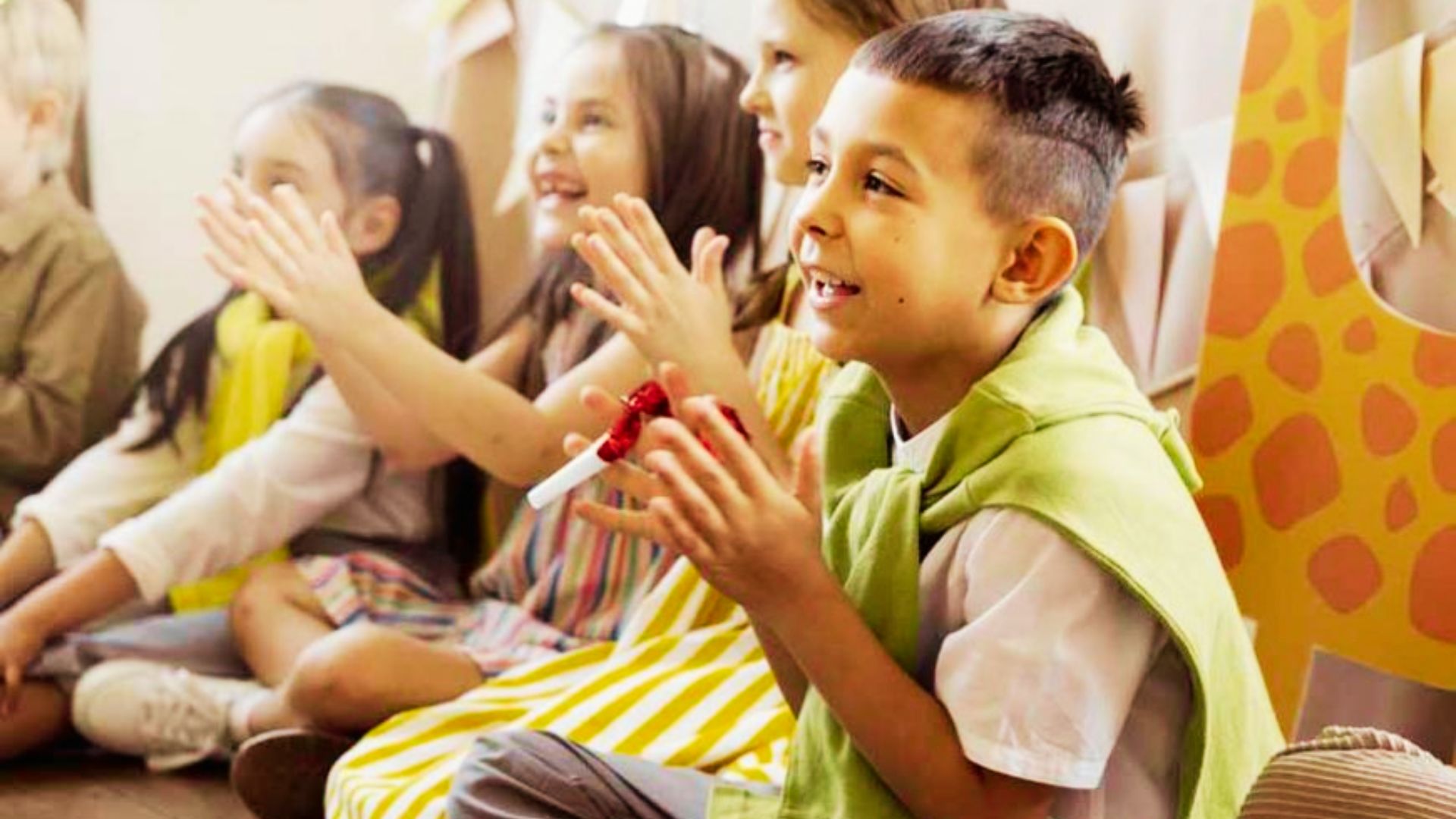 Children sitting on the floor, clapping and smiling joyfully during a fun activity.