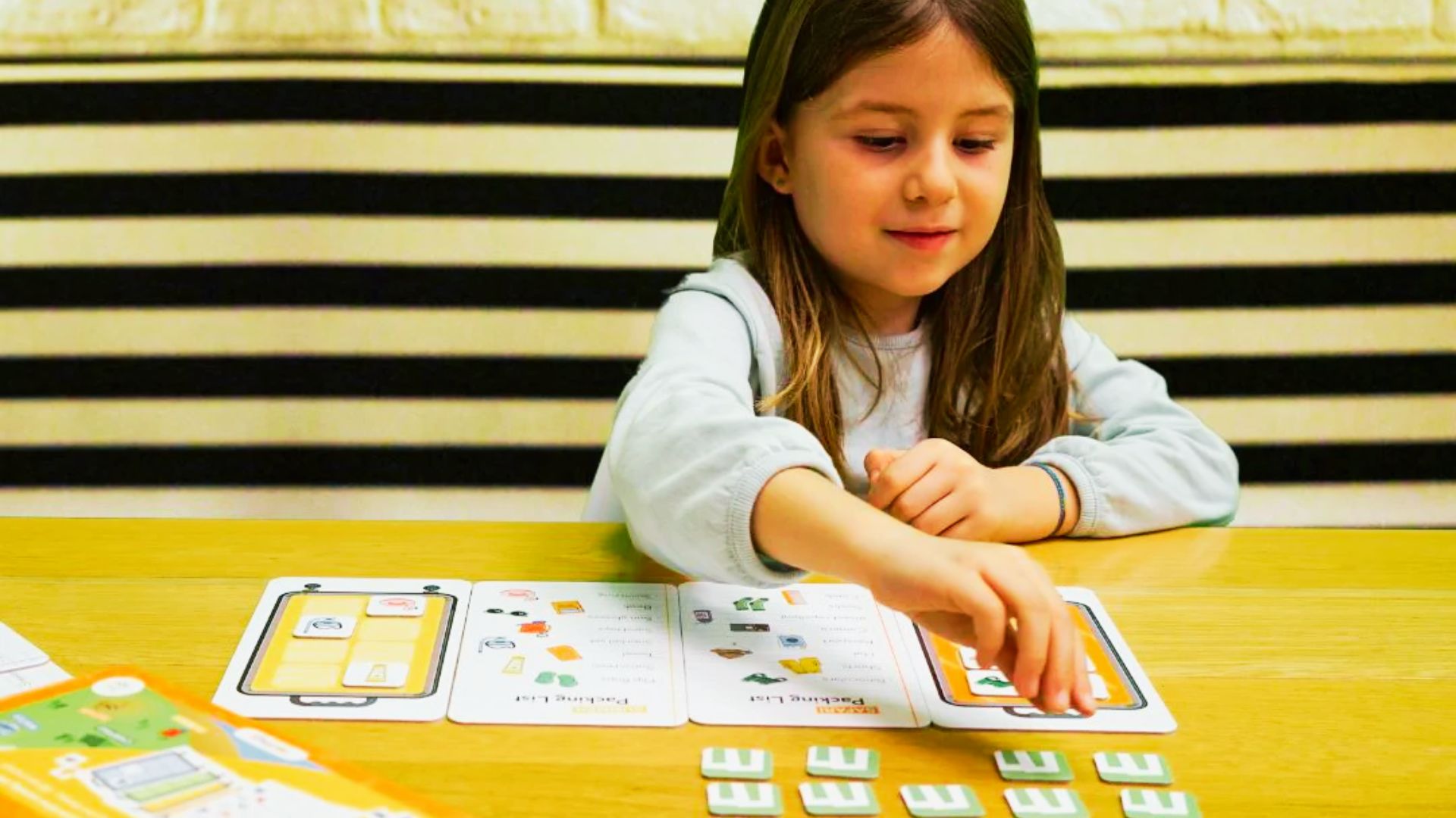 A young girl is focused on playing with a colorful game board, surrounded by game pieces and cards.
