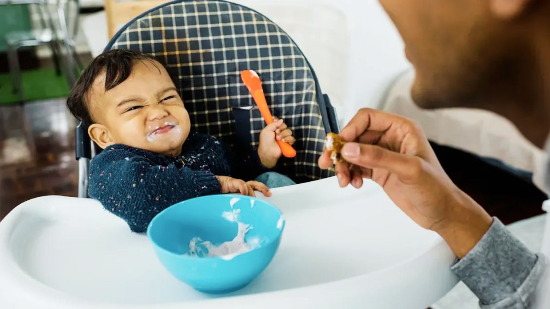 A man gently feeds a baby with a spoon, illustrating the concept of baby-led weaning versus purees.
