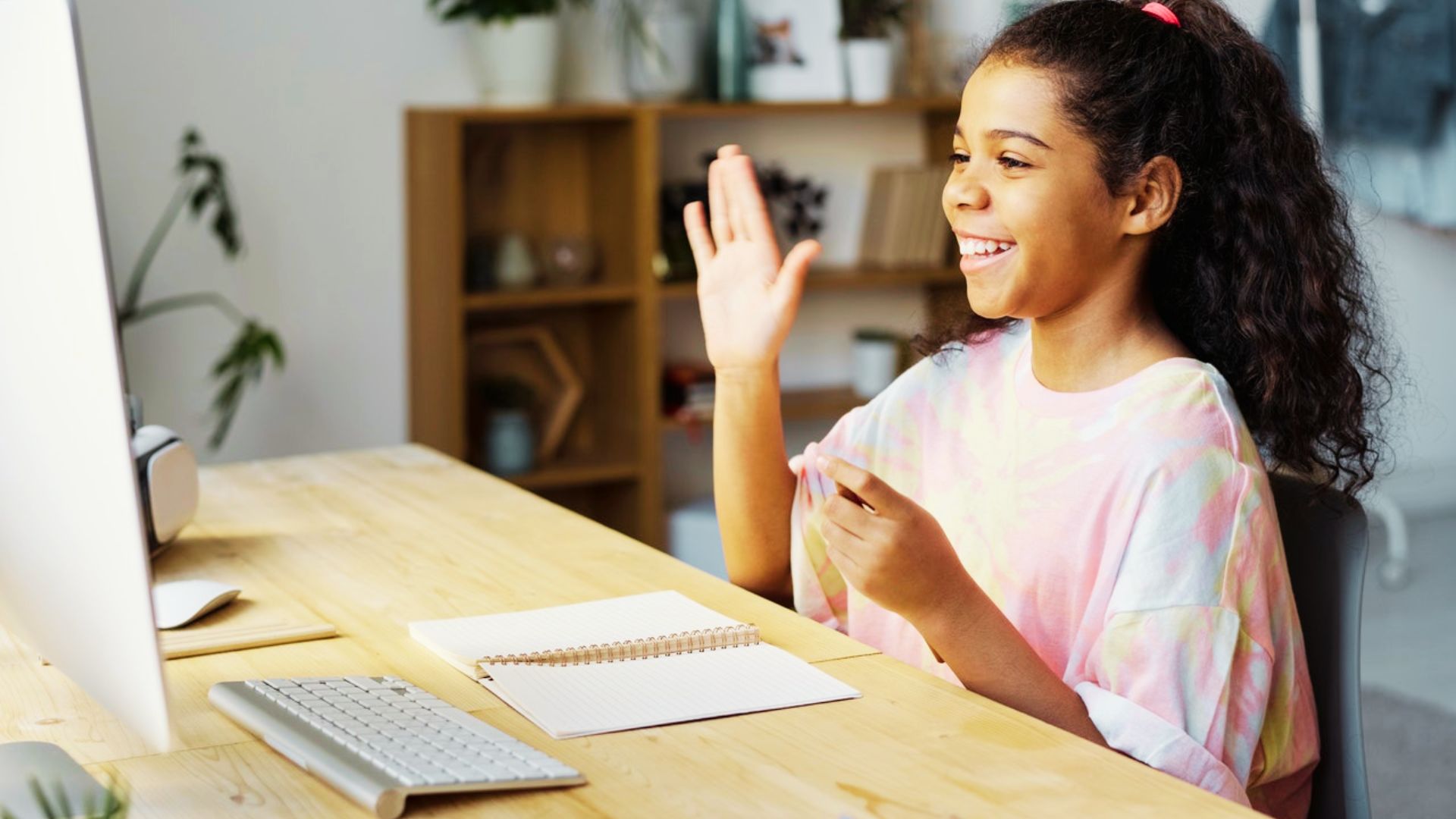 A young girl sitting at a desk with her hands raised, engaged in a problem-solving activity for teens.