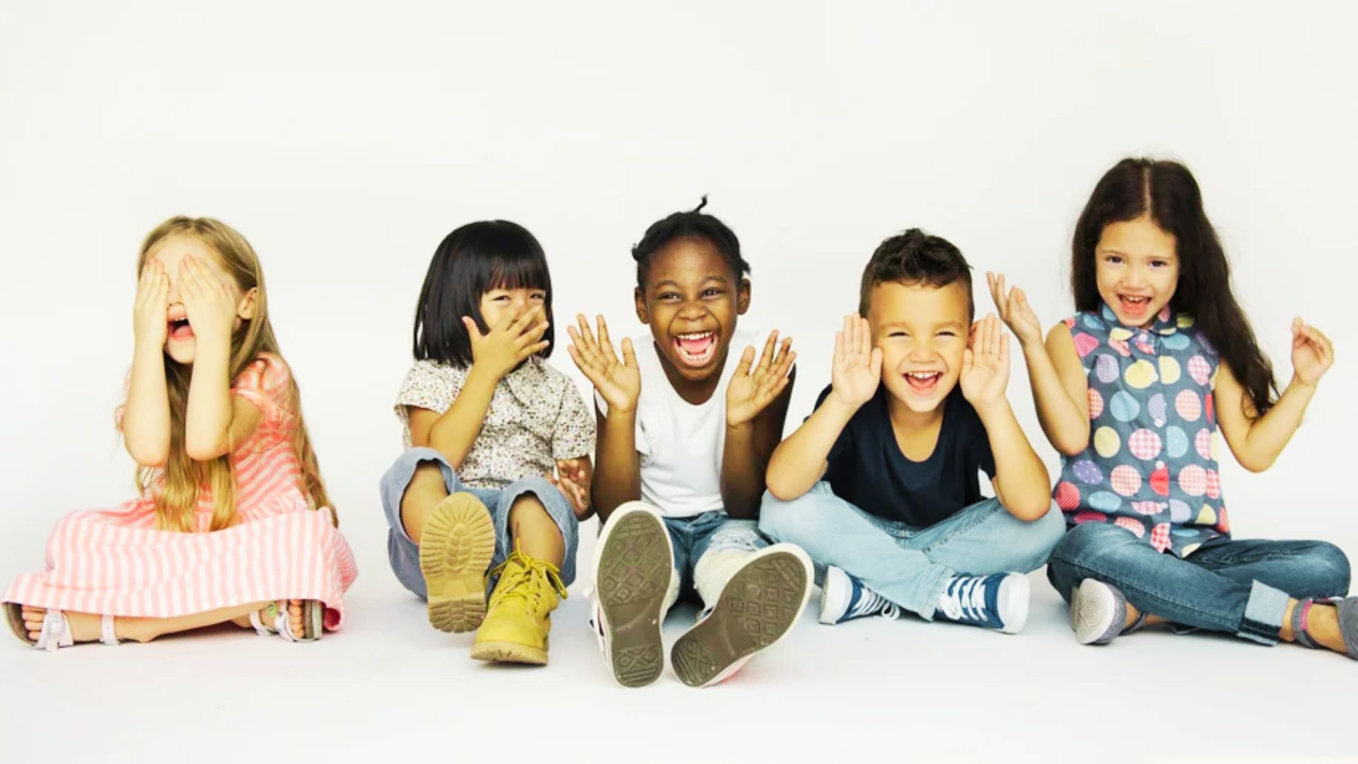 A group of children sitting on the floor, eagerly raising their hands in a classroom setting.