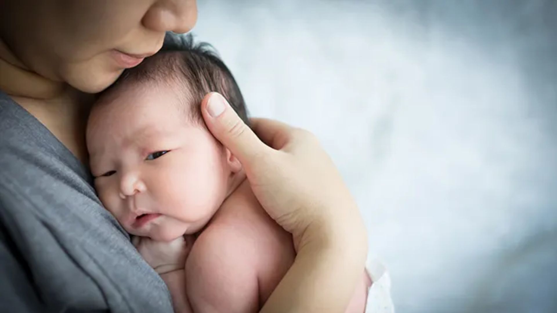 Close-up of skin-to-skin chest hold: Newborn rests against adult's chest with adult's hand gently supporting the baby's head and neck for safety and bonding.