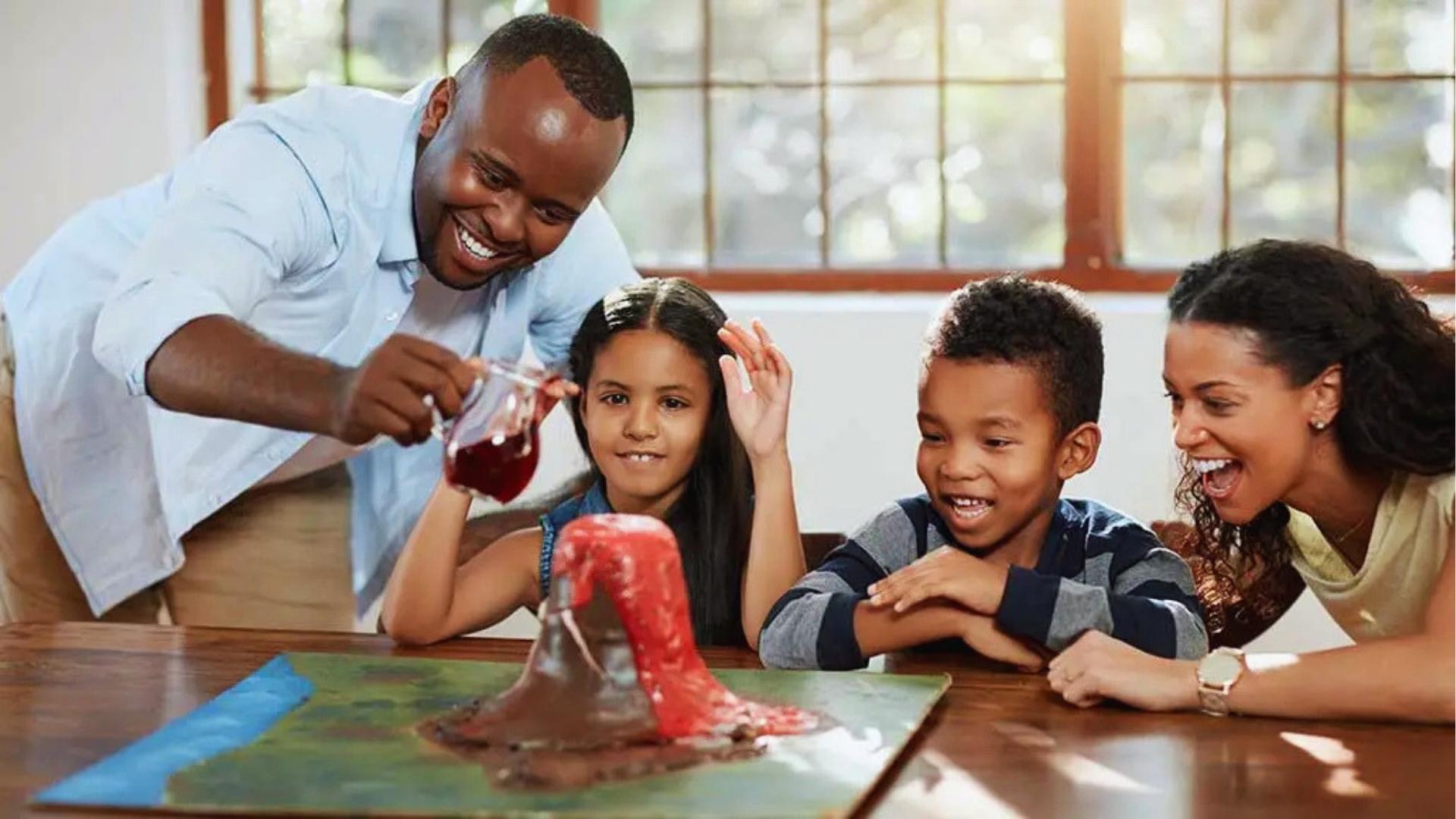 Family of four watches baking soda volcano erupt on table, laughing, science experiment.