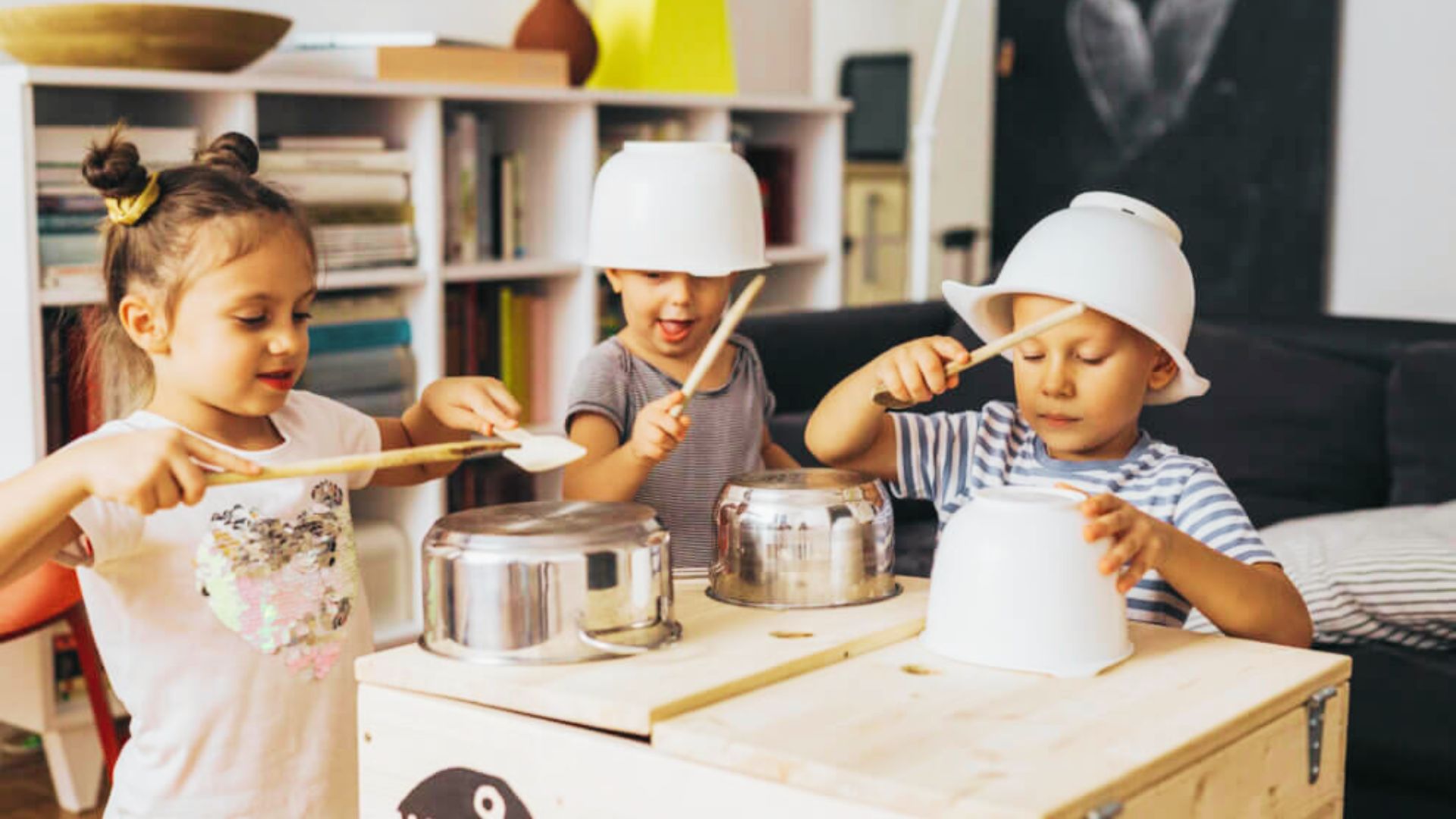 Three children joyfully playing with pots and pans in a bright kitchen, creating a lively and playful atmosphere.