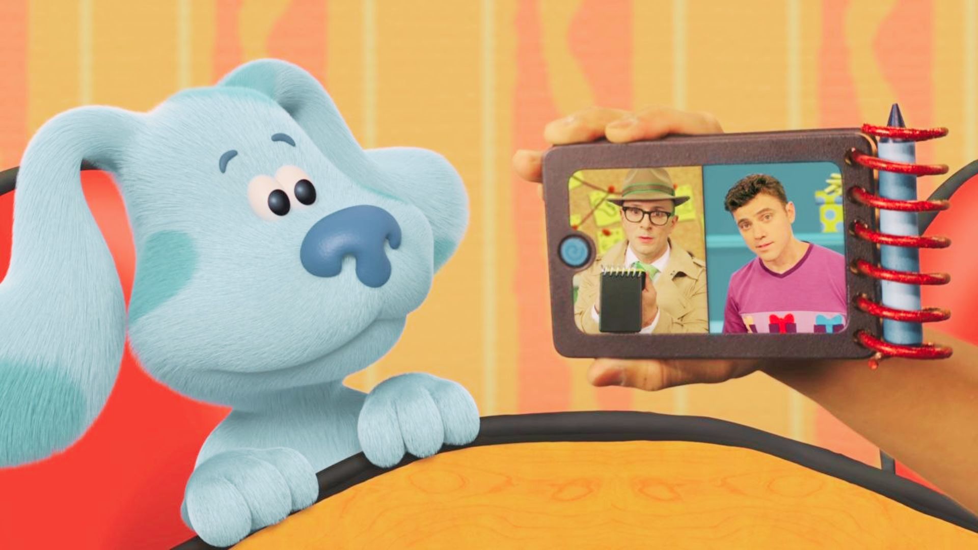 Blue, the dog from Blue's Clues, holds a tablet showing image of two men together.