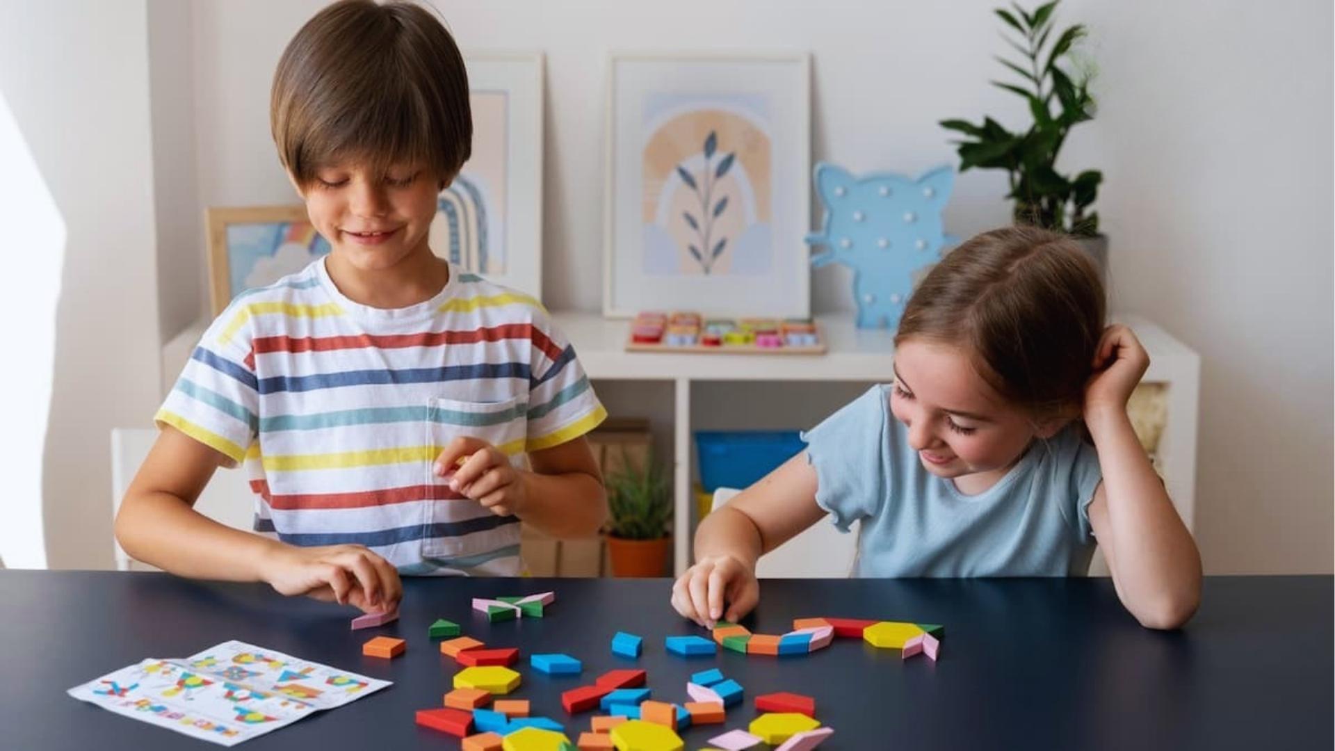 Two focused kids build shapes with colorful geometric tiles at dark table, instruction sheet, Activities for Autistic Kids.