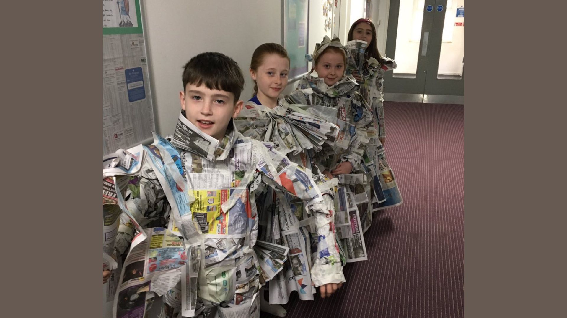 Four kids standing in a school hallway wearing creative costumes made from newspaper, showing a fun recycled art group activity for kids at school