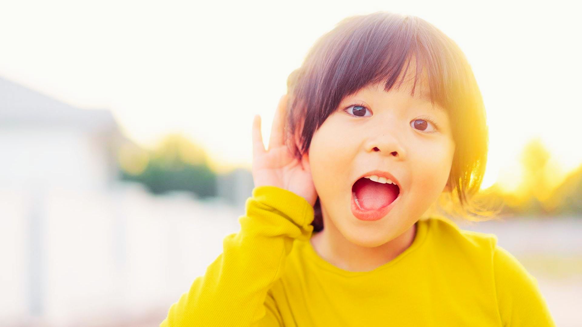 A little girl wearing a yellow shirt, with her mouth open in surprise or excitement.