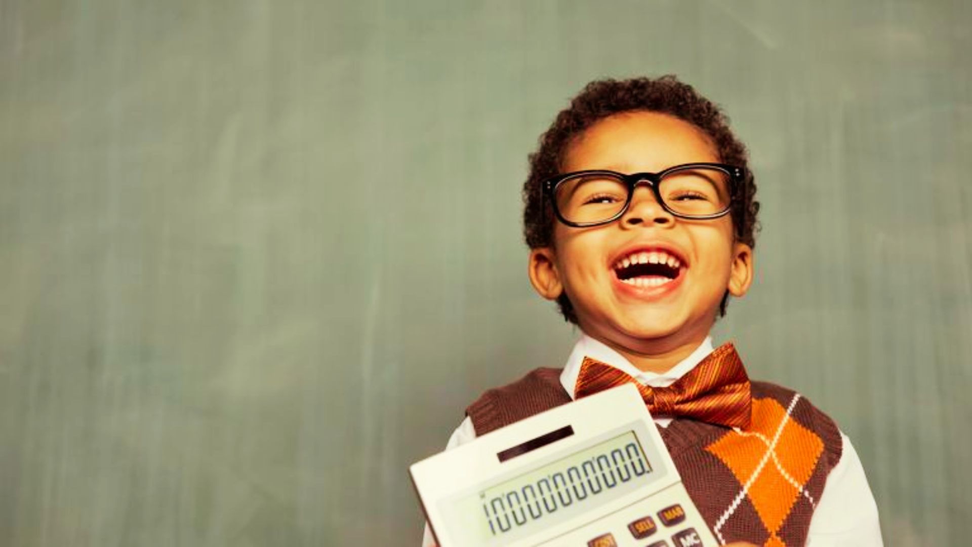 A young boy with glasses and a vest is holding a calculator.