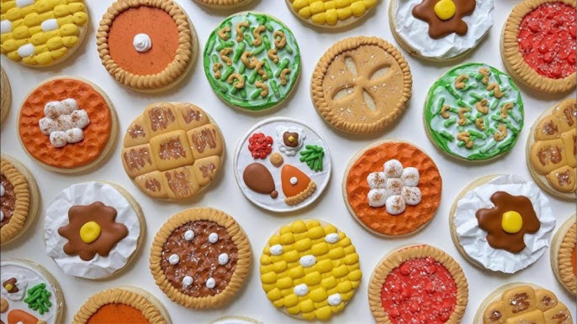 Assortment of decorated cookies shaped like pies, corn, eggs, waffles, detailed icing designs.