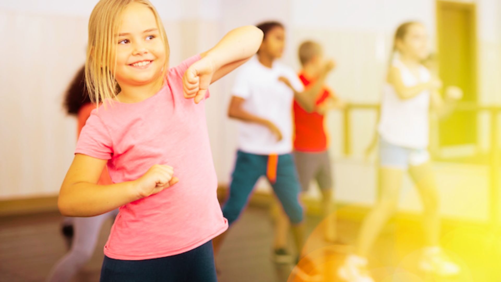 A young girl joyfully dances in a dance class, surrounded by her other kids.