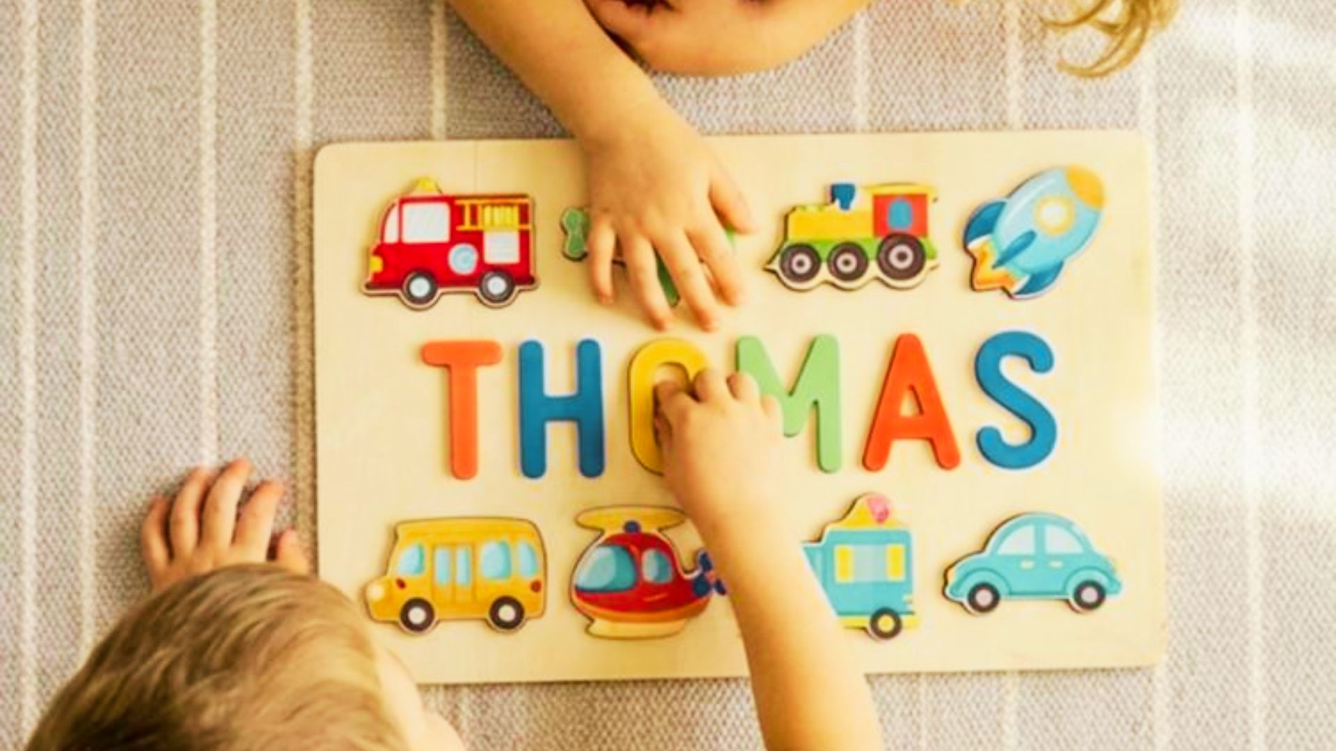 Two children engaged in play with a wooden puzzle featuring the name "Thomas" prominently displayed.