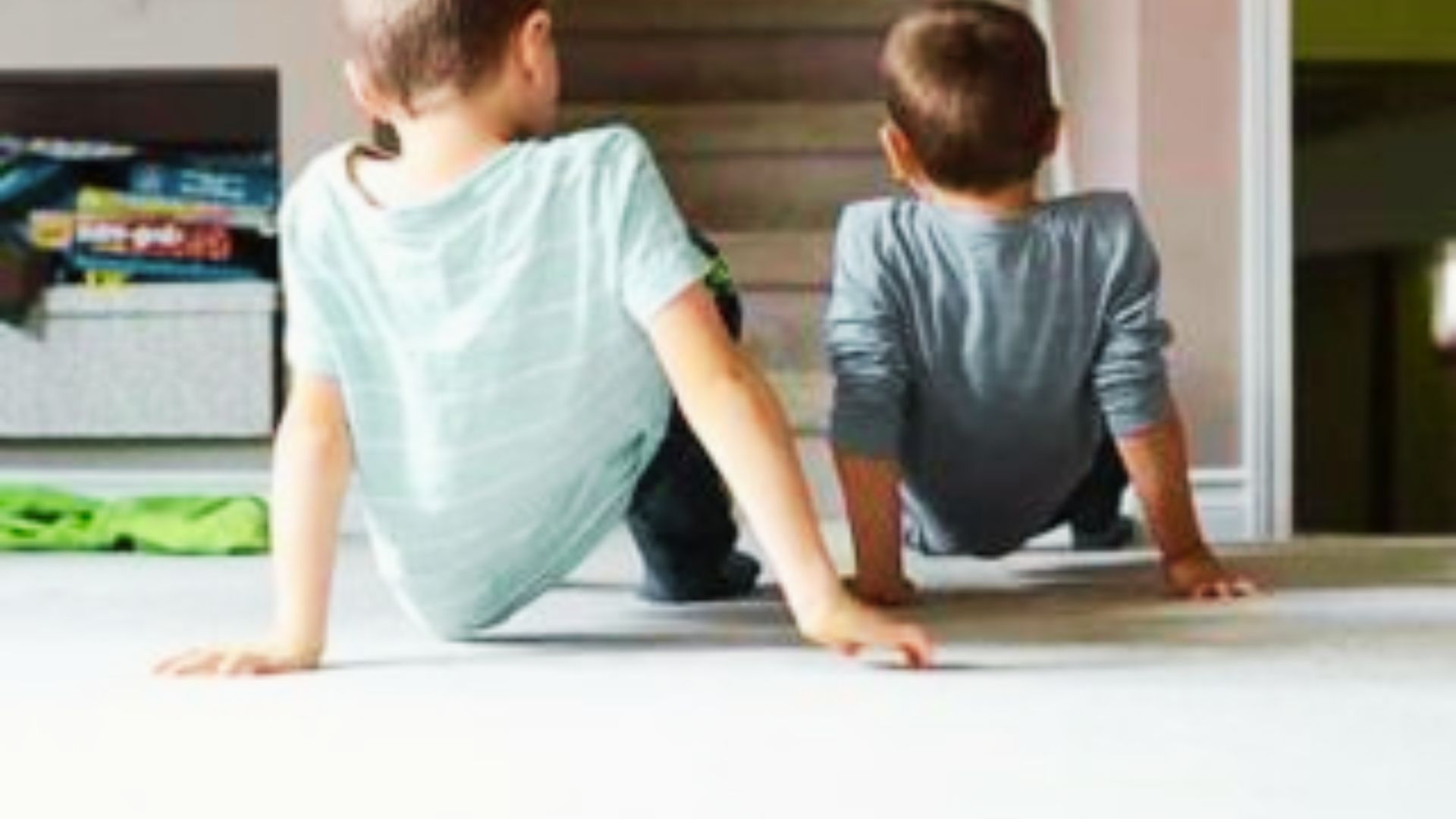 Two boys doing animal walk on the floor, leaning against a door, engaged in conversation.