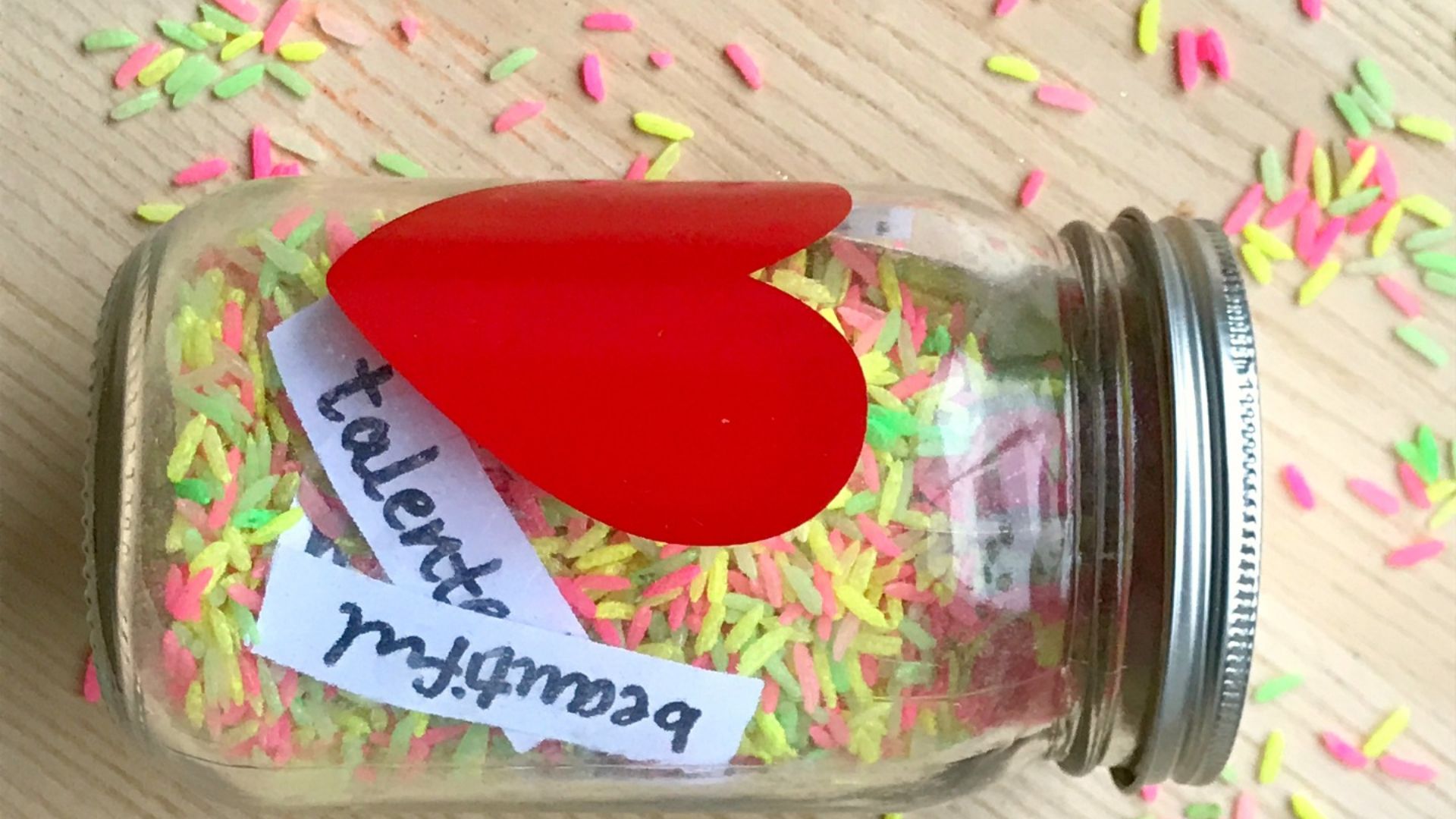 Friendship compliment jar filled with colorful rice and positive word strips like beautiful and talented, used for kindness and affirmation activities for preschoolers