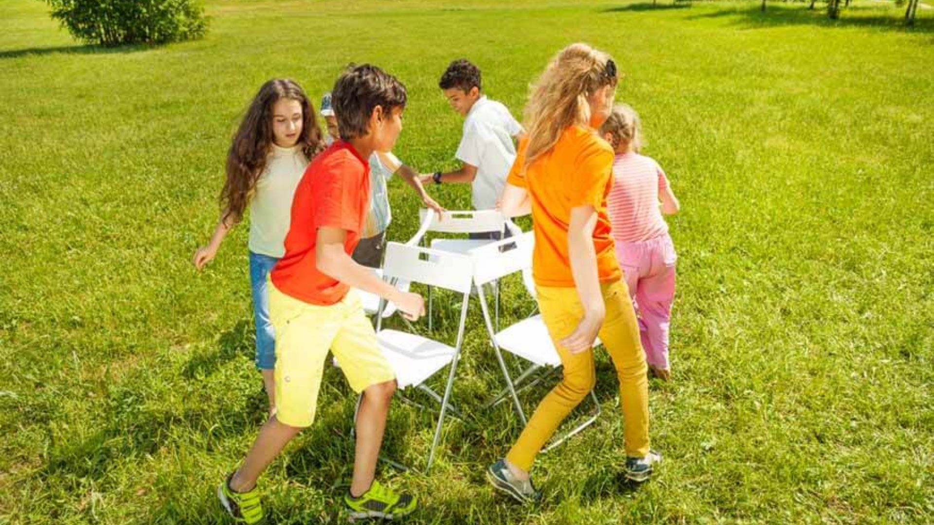 Group of preschoolers playing musical chairs together on a sunny lawn, practicing turn-taking and good sportsmanship in a group friendship activity for kids