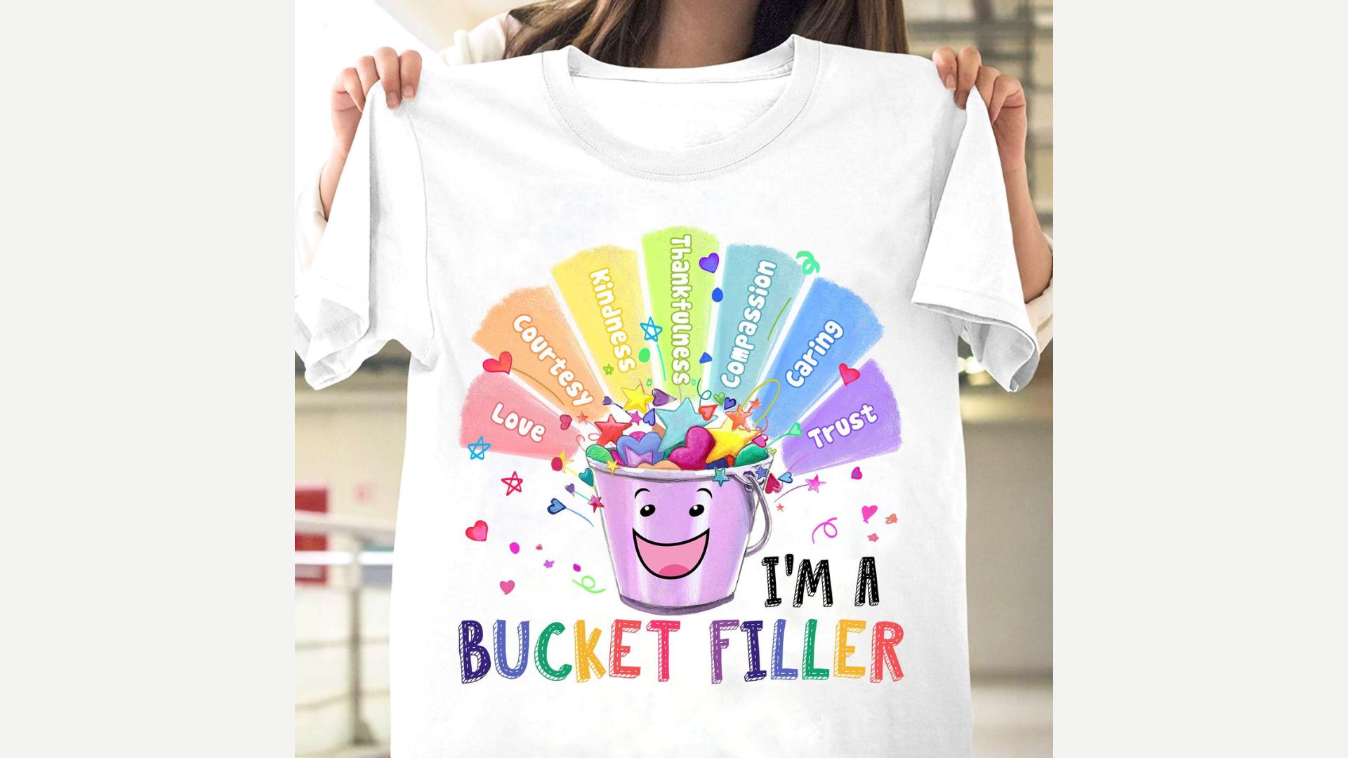 White t-shirt with colorful “I’M A BUCKET FILLER” graphic showing a smiling purple bucket and rainbow.