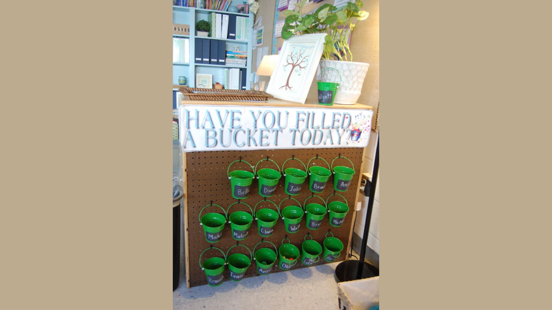 Classroom pegboard display with green mini buckets labeled with student names under a “HAVE YOU FILLED A BUCKET TODAY?” sign.