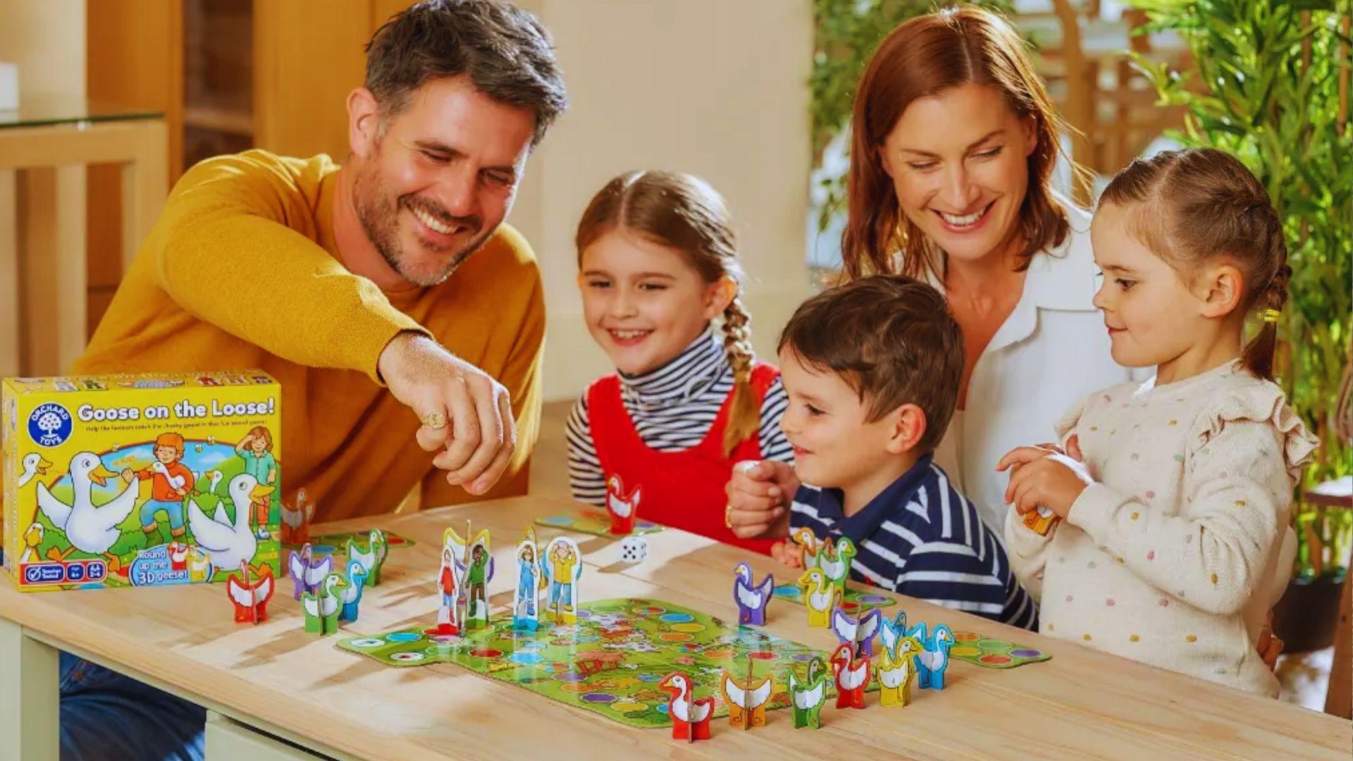 A family enjoys a board game together, smiling and engaging with their children around a table.