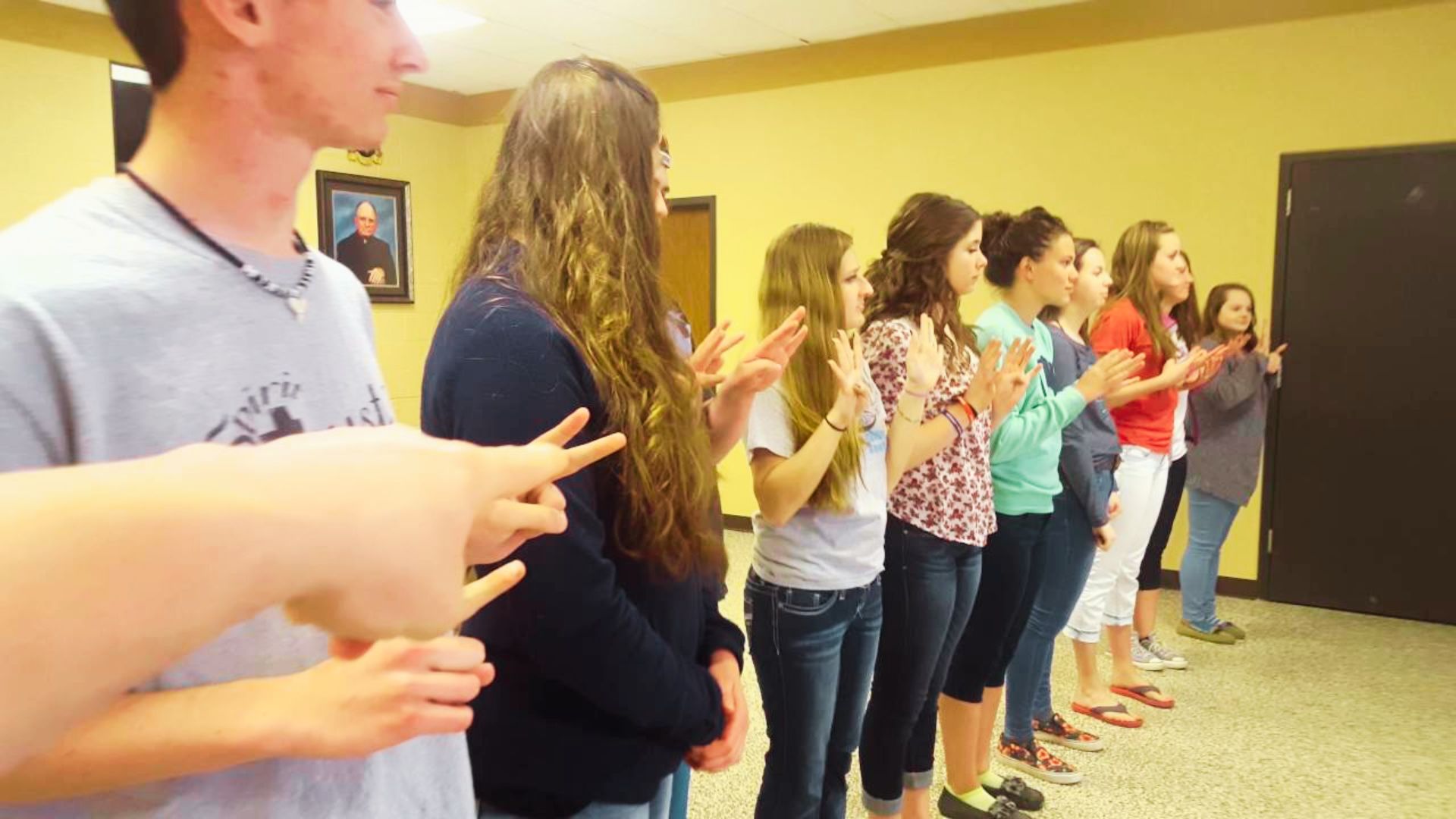 A group of people standing in a line, doing hand gestures.