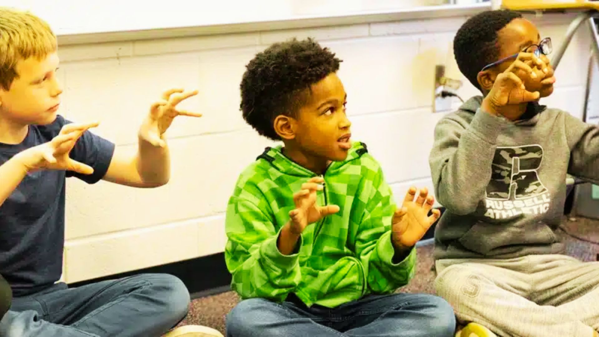 Three boys seated on the floor, hands raised enthusiastically, capturing a moment of fun and interaction.