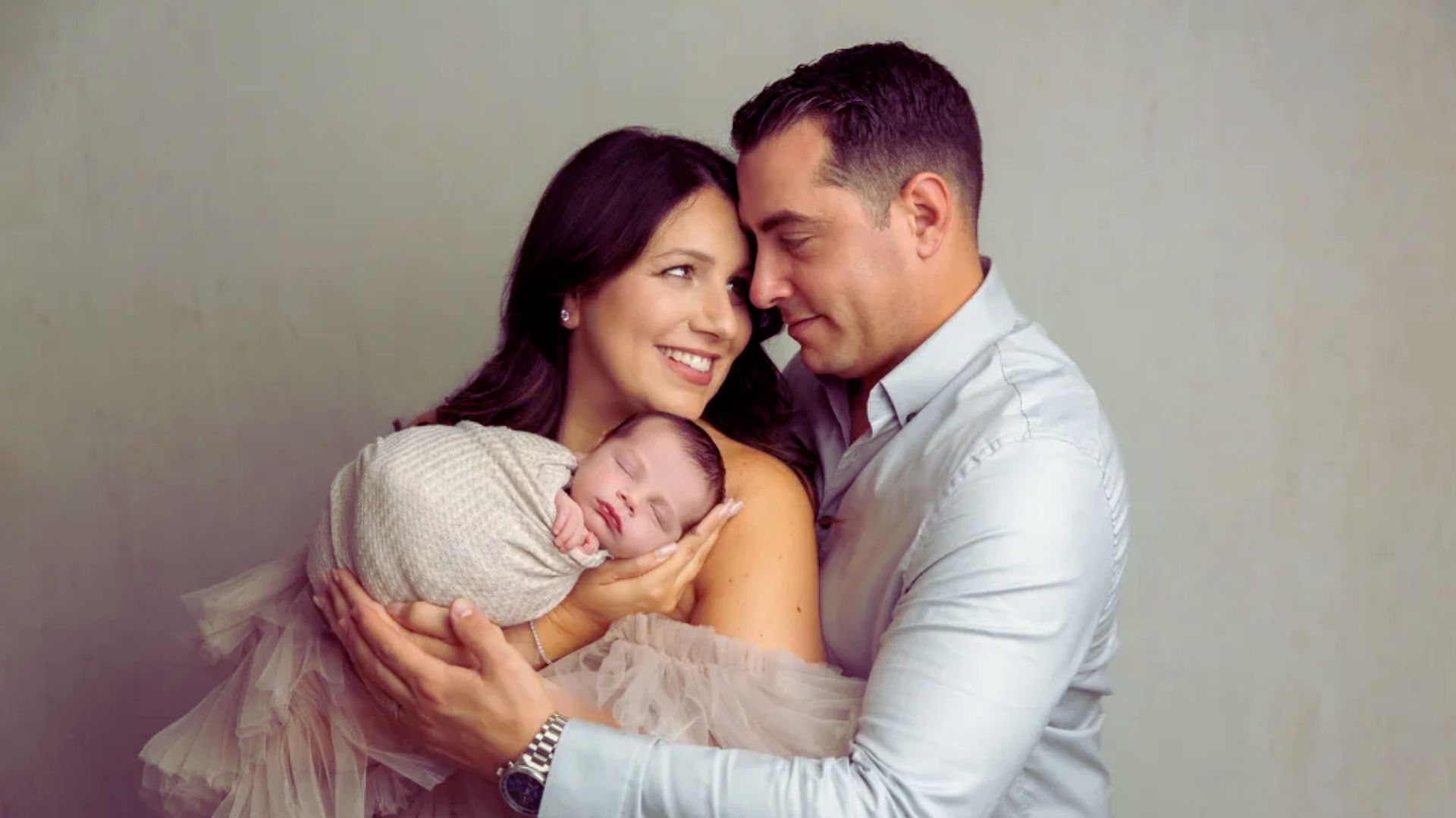 A man and woman lovingly hold their newborn daughter, smiling at each other in a moment of joy and tenderness.