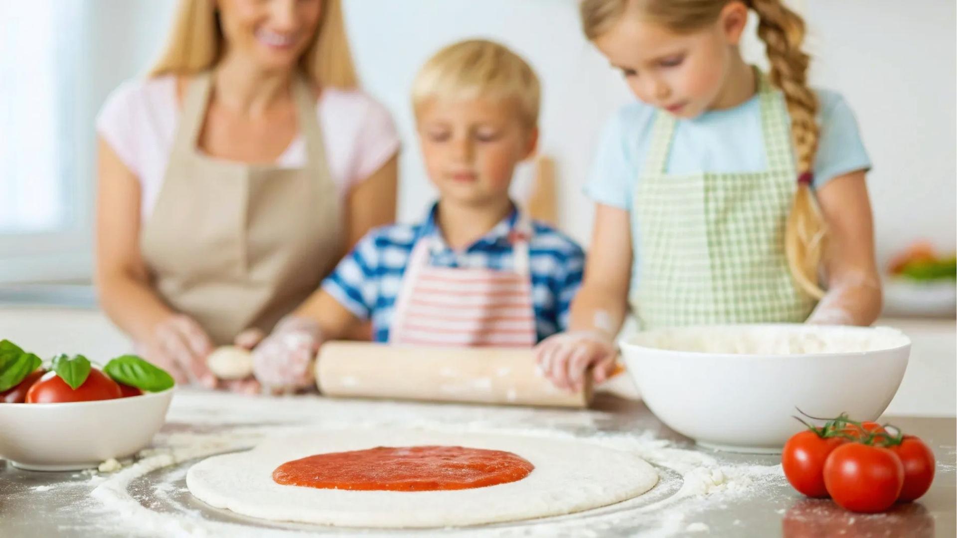 Mom and two kids in aprons roll pizza dough, sauce, tomatoes, flour, kitchen.