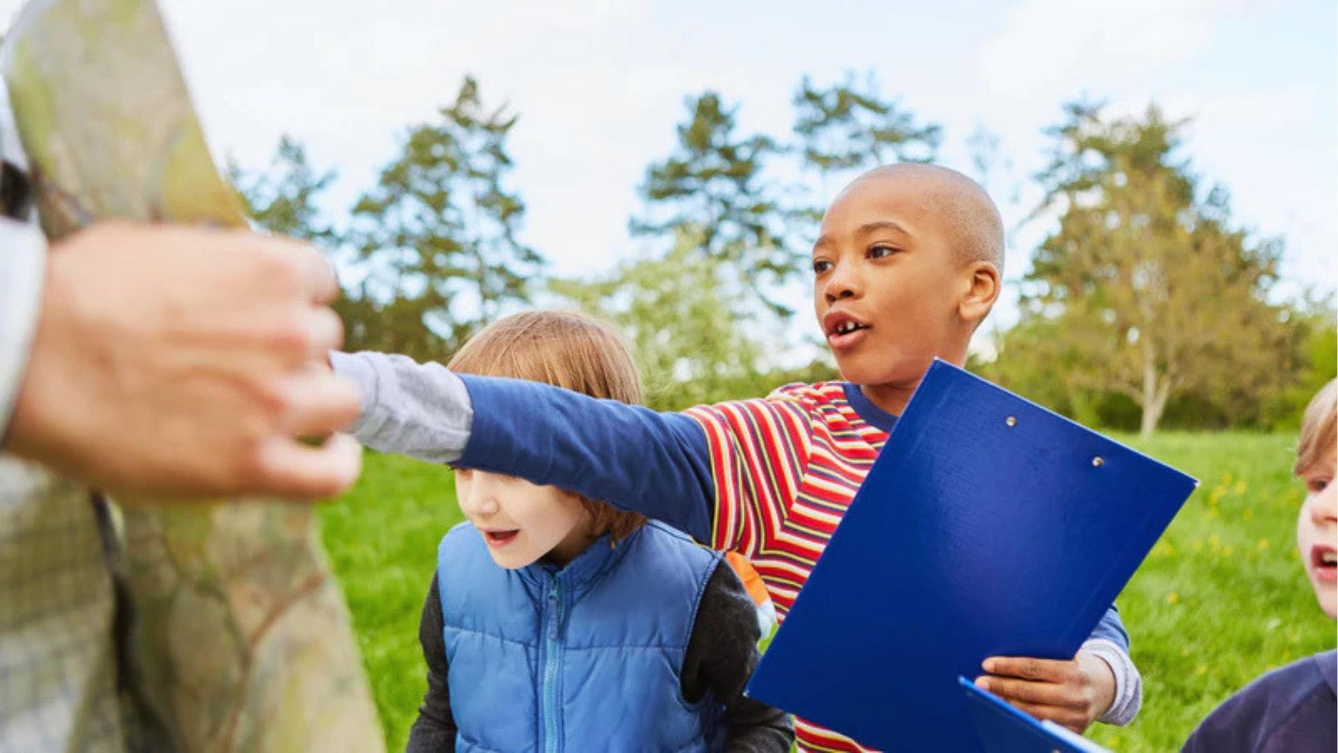 Boy holds blue clipboard pointing at map with kids