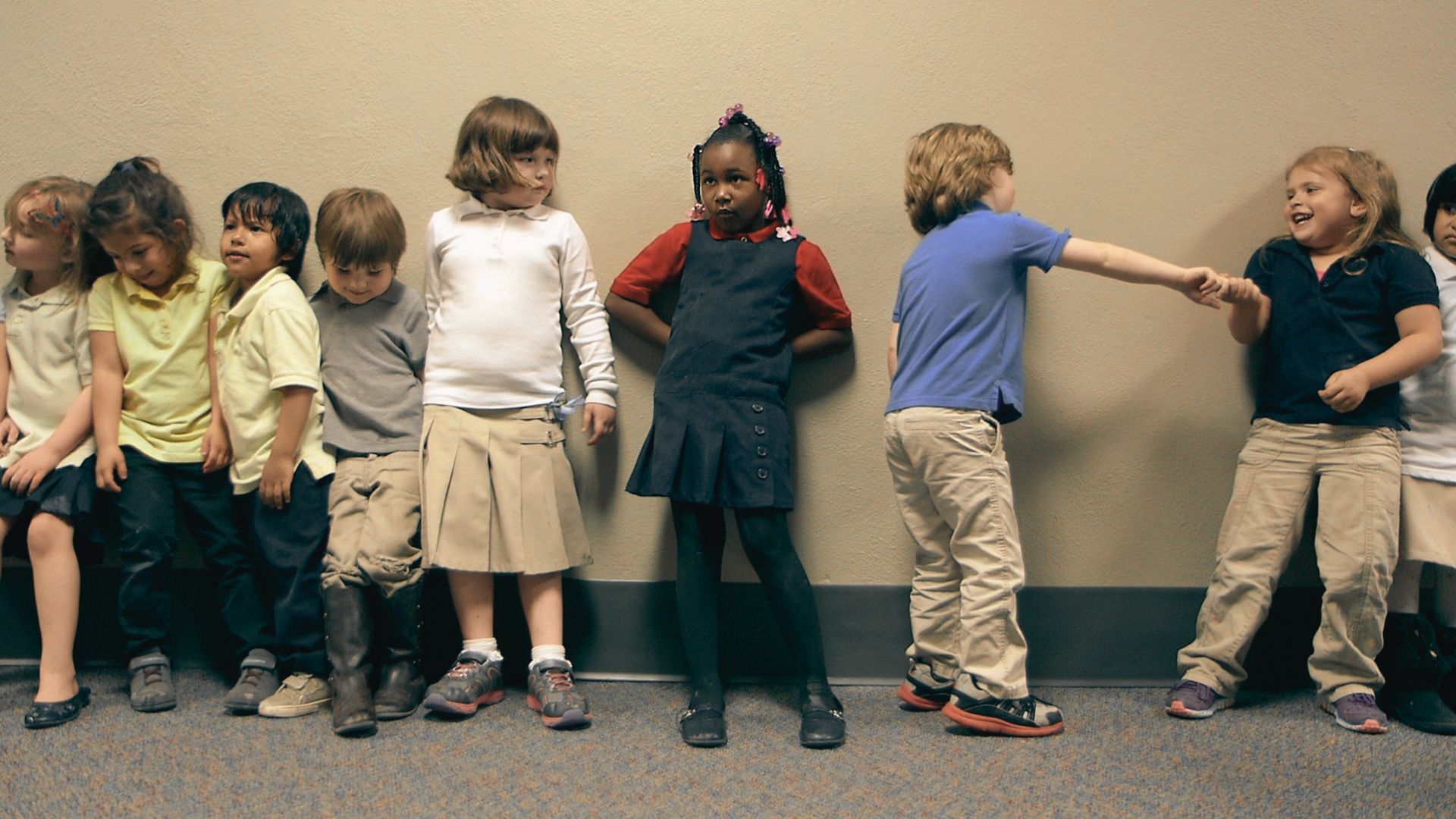 Several children lined up, looking towards the camera, with a variety of hairstyles and outfits.
