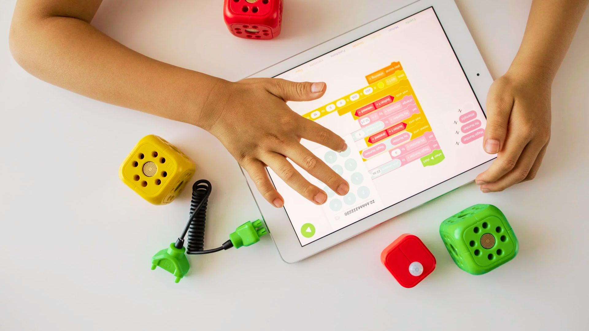 A child's hands touch a tablet displaying vibrant, colorful building blocks on the screen.