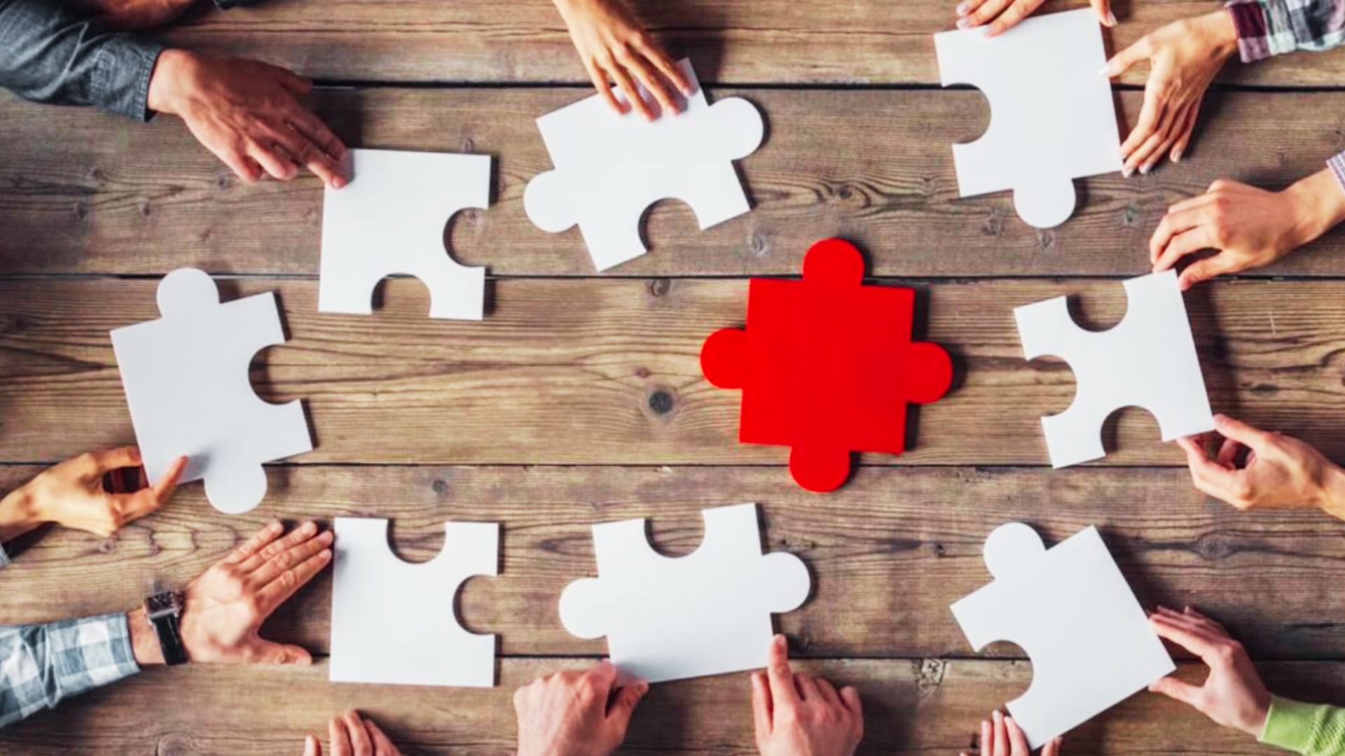 People collaboratively fitting puzzle pieces together on a wooden table, showcasing teamwork and problem-solving.