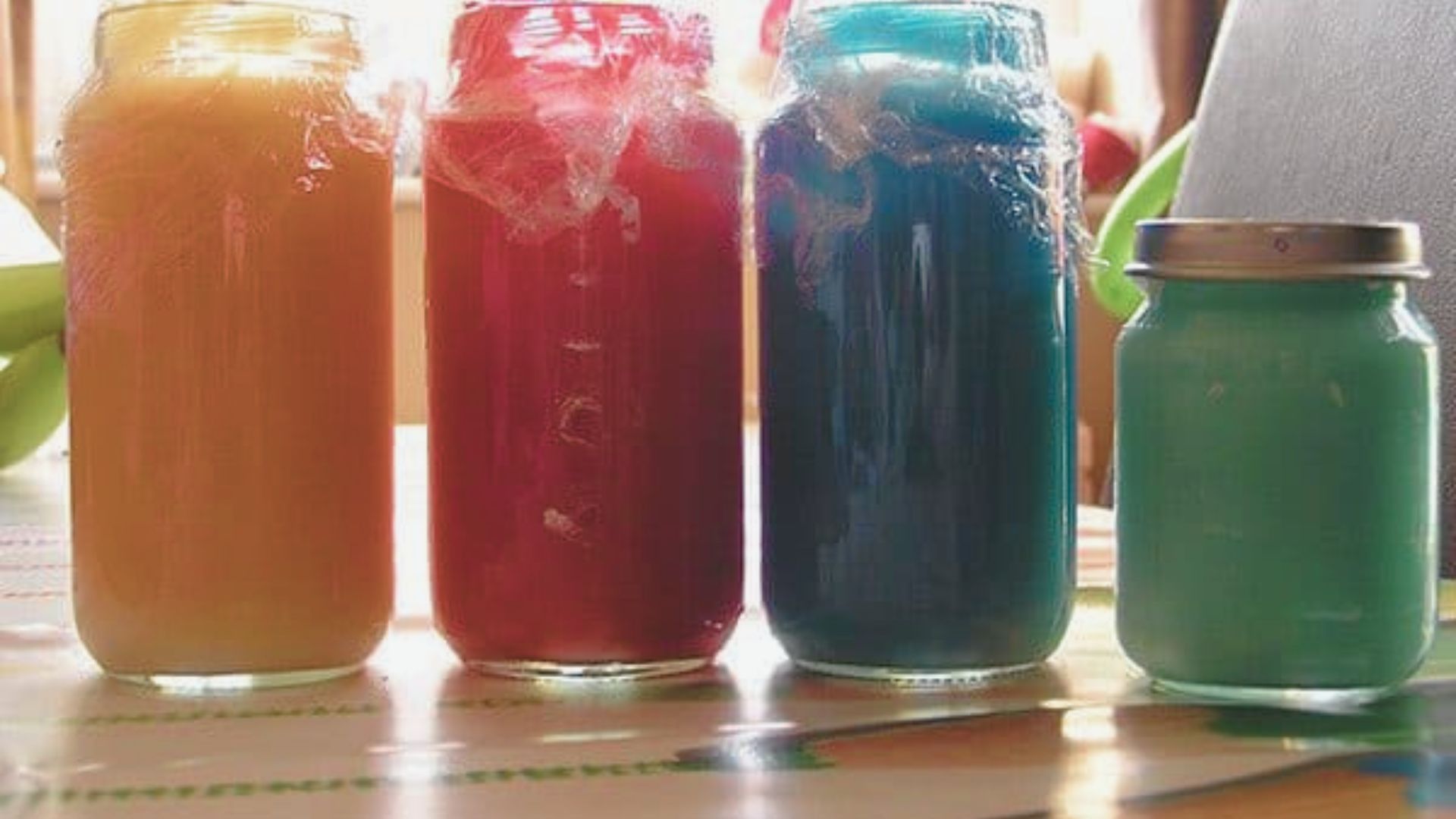 Four glass jars hold brightly colored homemade finger paints in shades of orange, red, blue, and green.