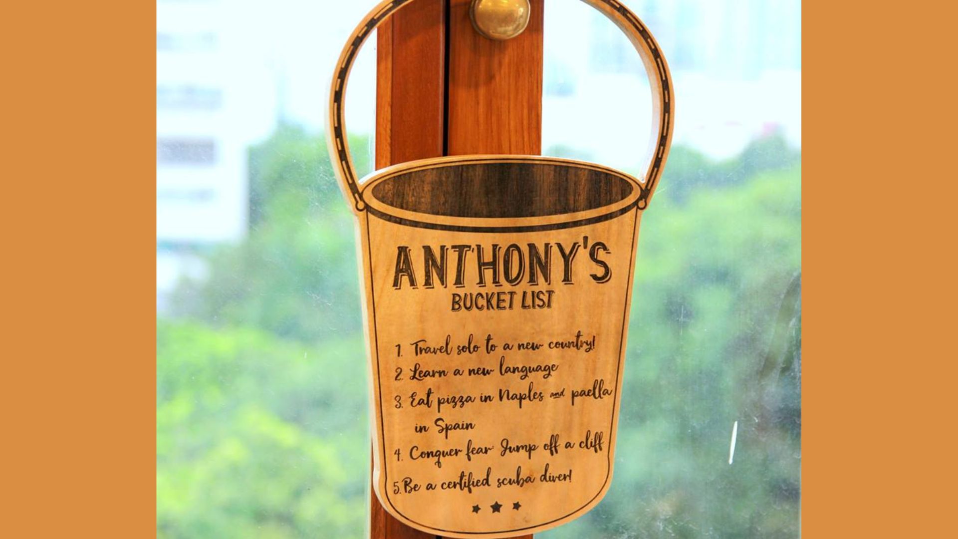 Wooden bucket-shaped door hanger labeled “ANTHONY’S BUCKET LIST” with goals like “Travel solo to a new country,” “Learn a new language,” and “Be a certified scuba diver.”