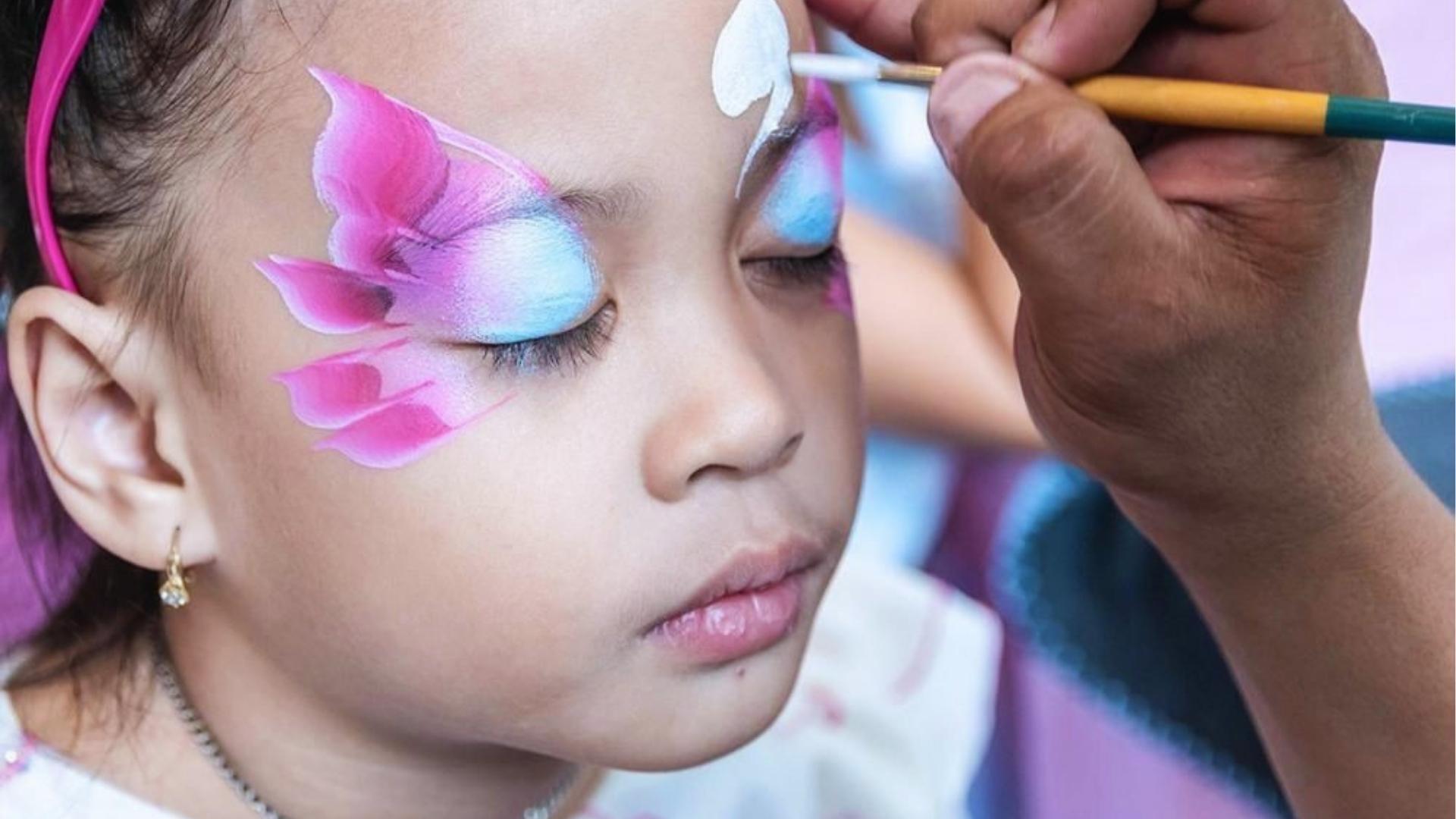 Close up of a girl getting pink and blue butterfly face paint, brush, artist.