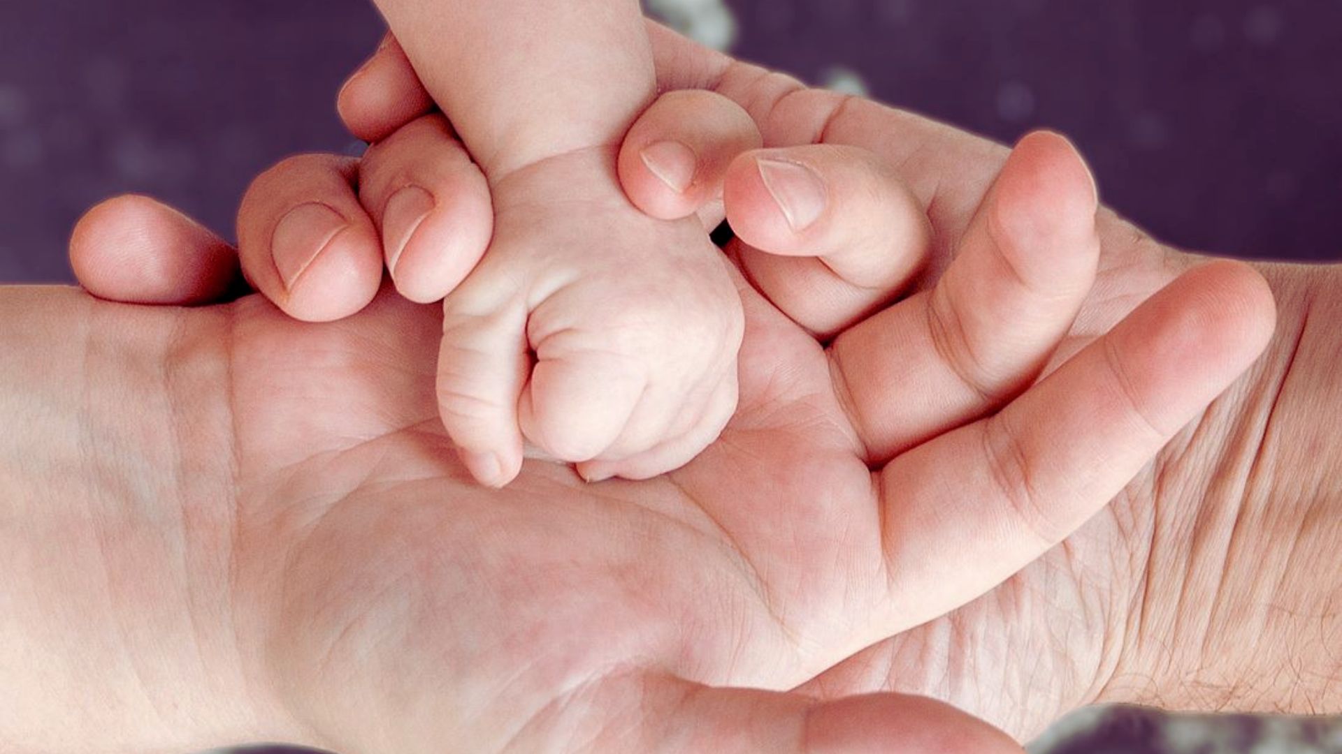 A close-up of a baby's hand gently grasping an adult's hand, symbolizing connection and tenderness.