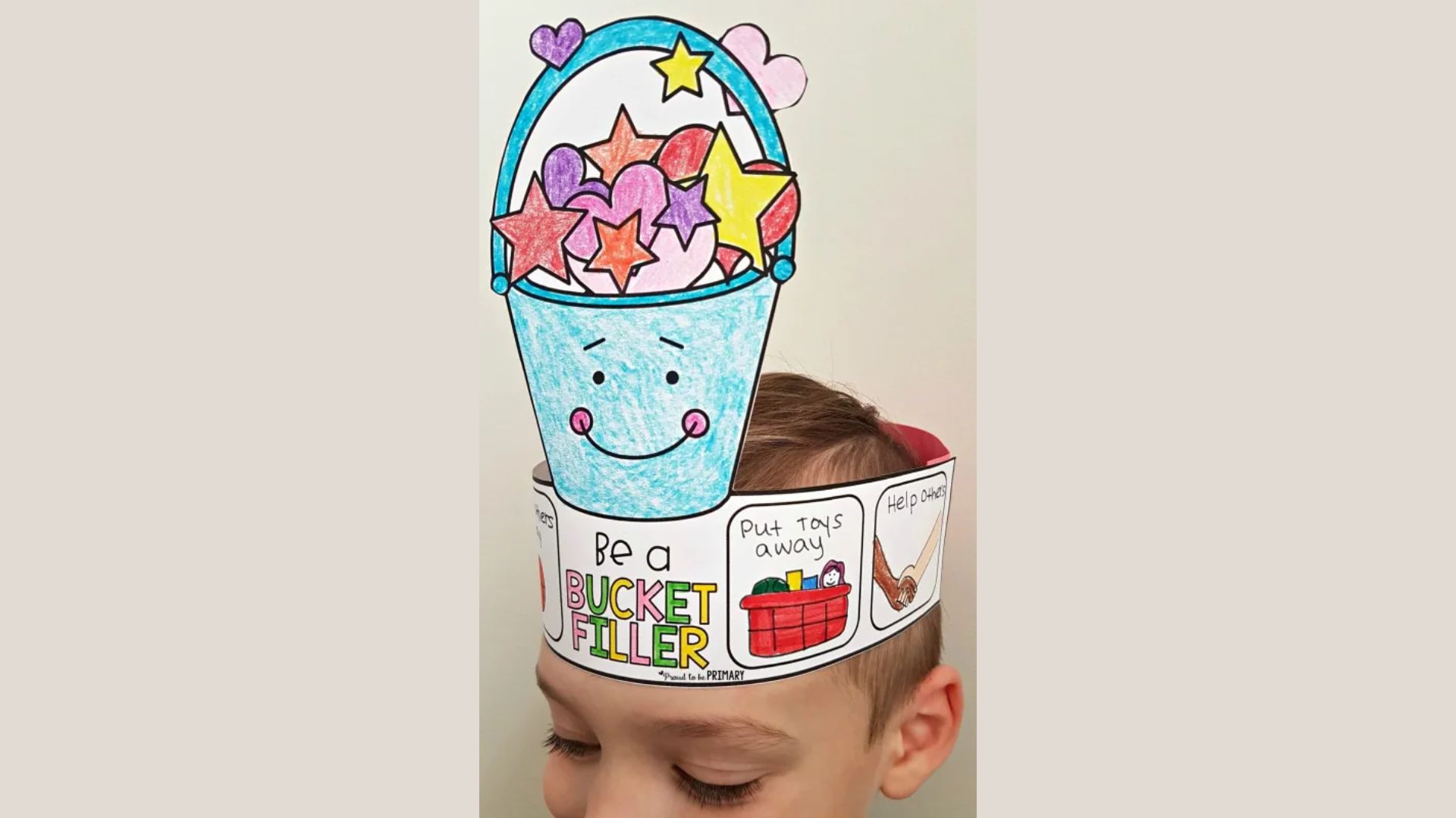Child wearing a handmade paper crown that reads “Be a BUCKET FILLER” with a smiling blue bucket filled with colored hearts and stars.