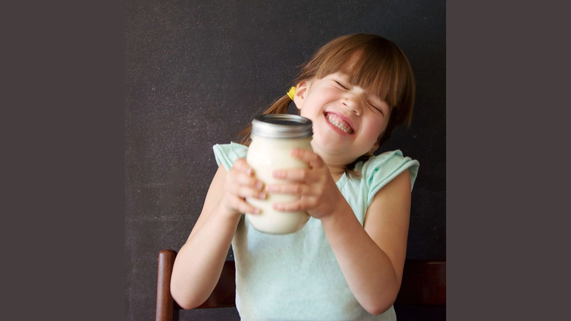 Happy girl shaking a mason jar filled with cream to make homemade butter, a farm-to-table food activity for kids