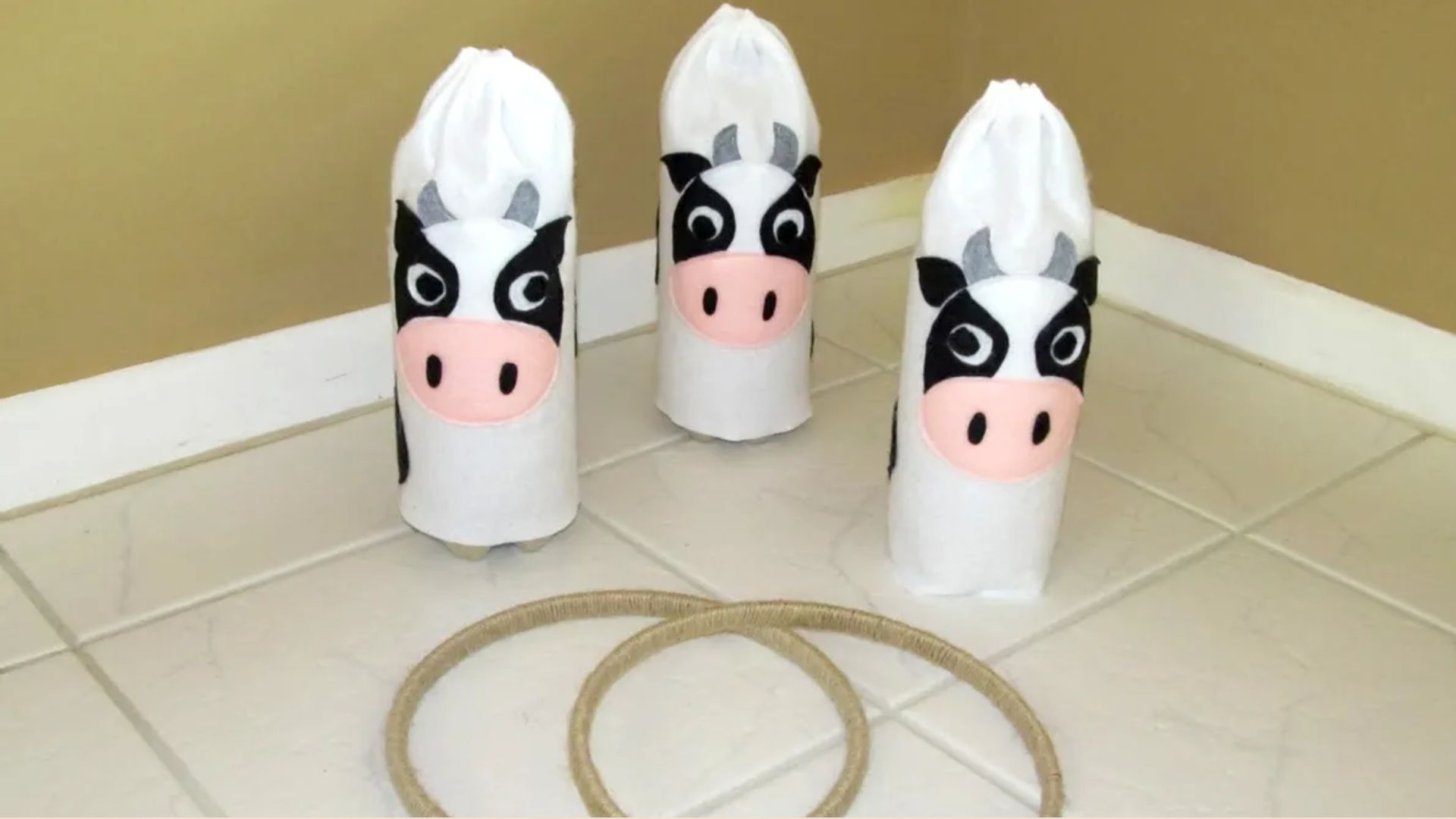 DIY cow ring toss game made with bottles decorated as cows and rope rings, an indoor farm party activity for kids