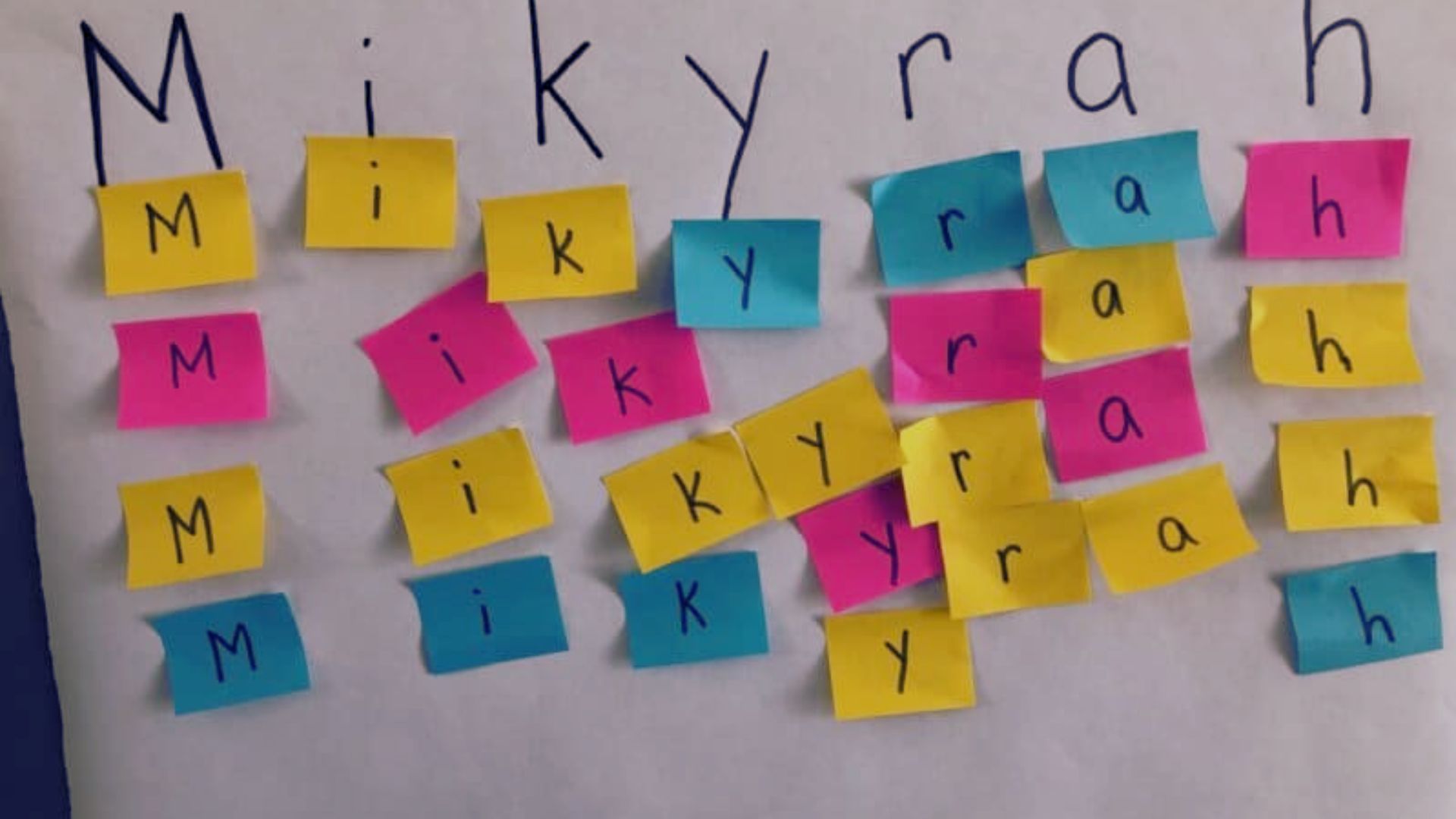 Colorful sticky notes spell out the name "Mikyrah" on paper, with multiple letter options for each character.