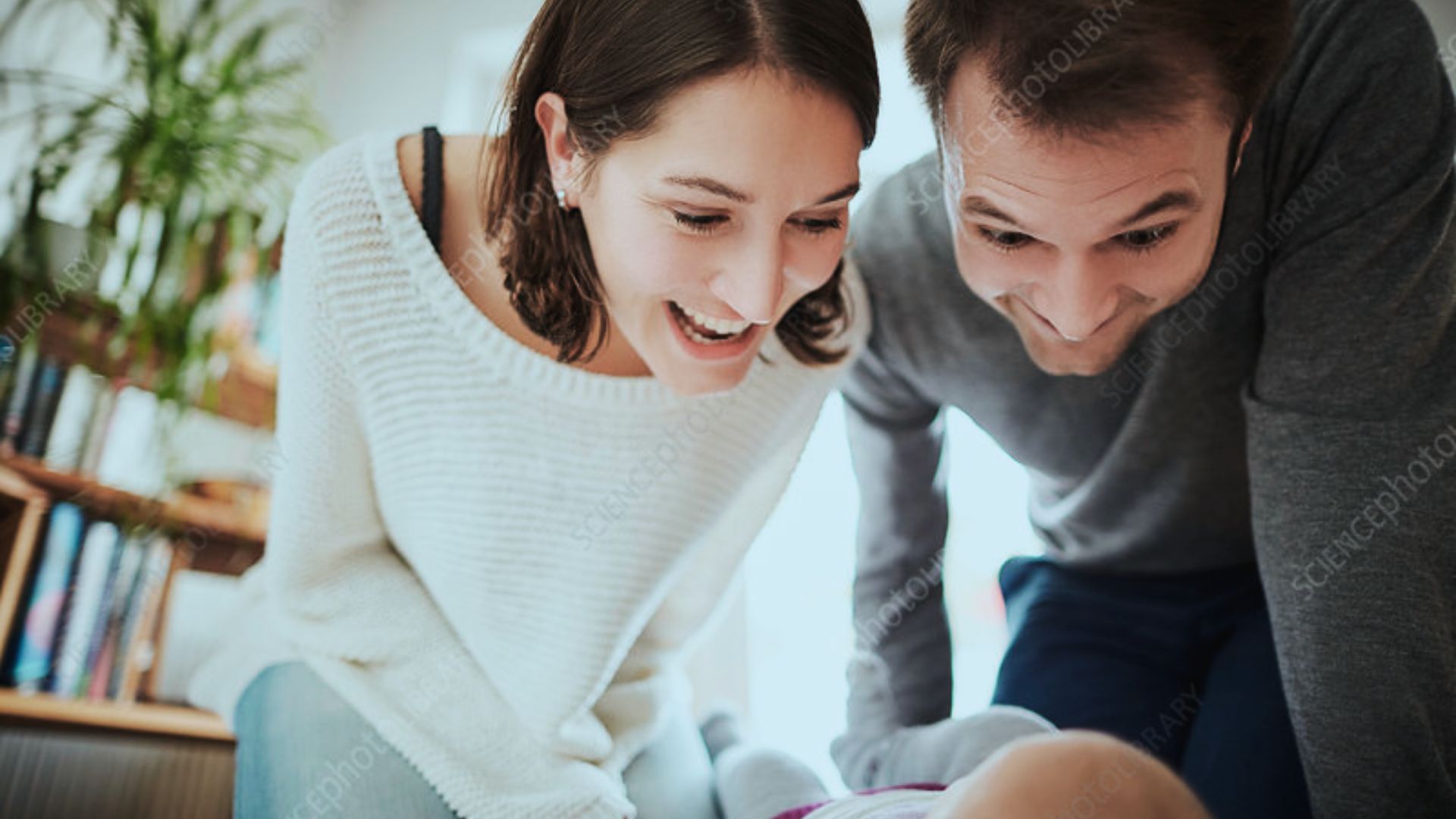 A smiling man and woman gaze lovingly at a baby in their arms, radiating joy and warmth.