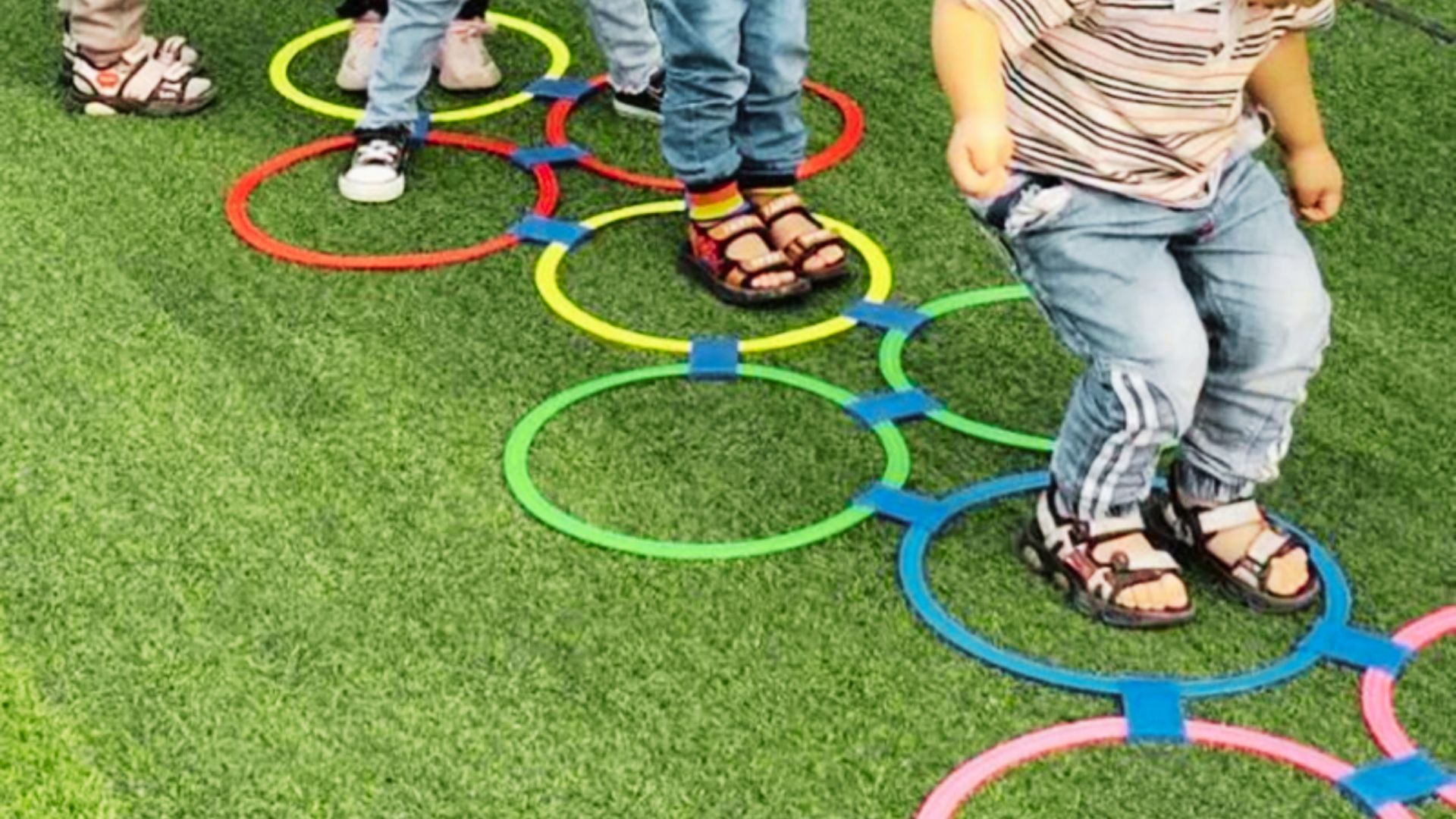 Children joyfully playing with colorful rings on a sunny grass field, surrounded by greenery and bright blue sky.