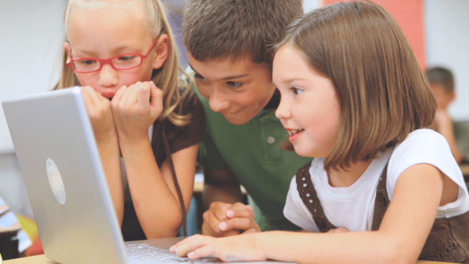Three elementary school children smiling and collaborating on a laptop for a self esteem building activity that encourages teamwork and shared success