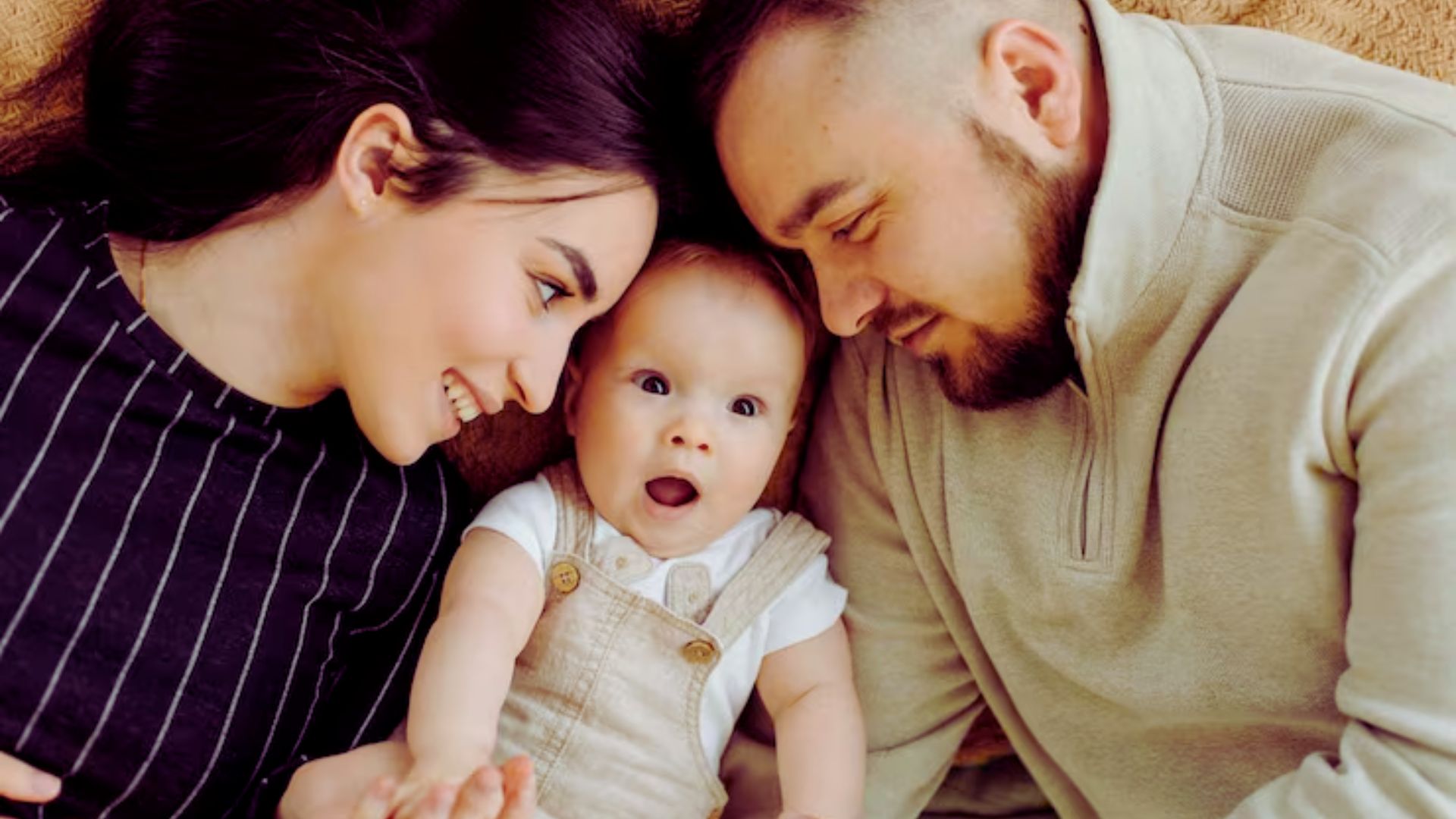 A man and woman recline on a couch, with a baby nestled comfortably in the woman's arms.