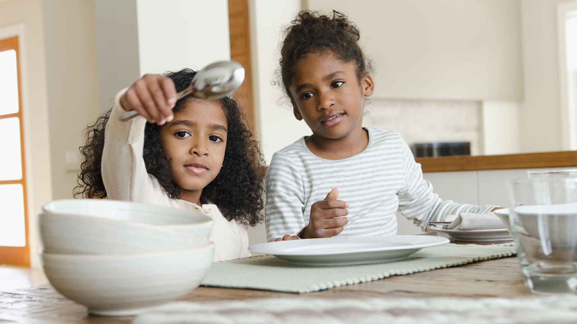 Two young girls proudly setting plates at a dining table, showing a responsibility based self esteem activity for kids that builds competence at home