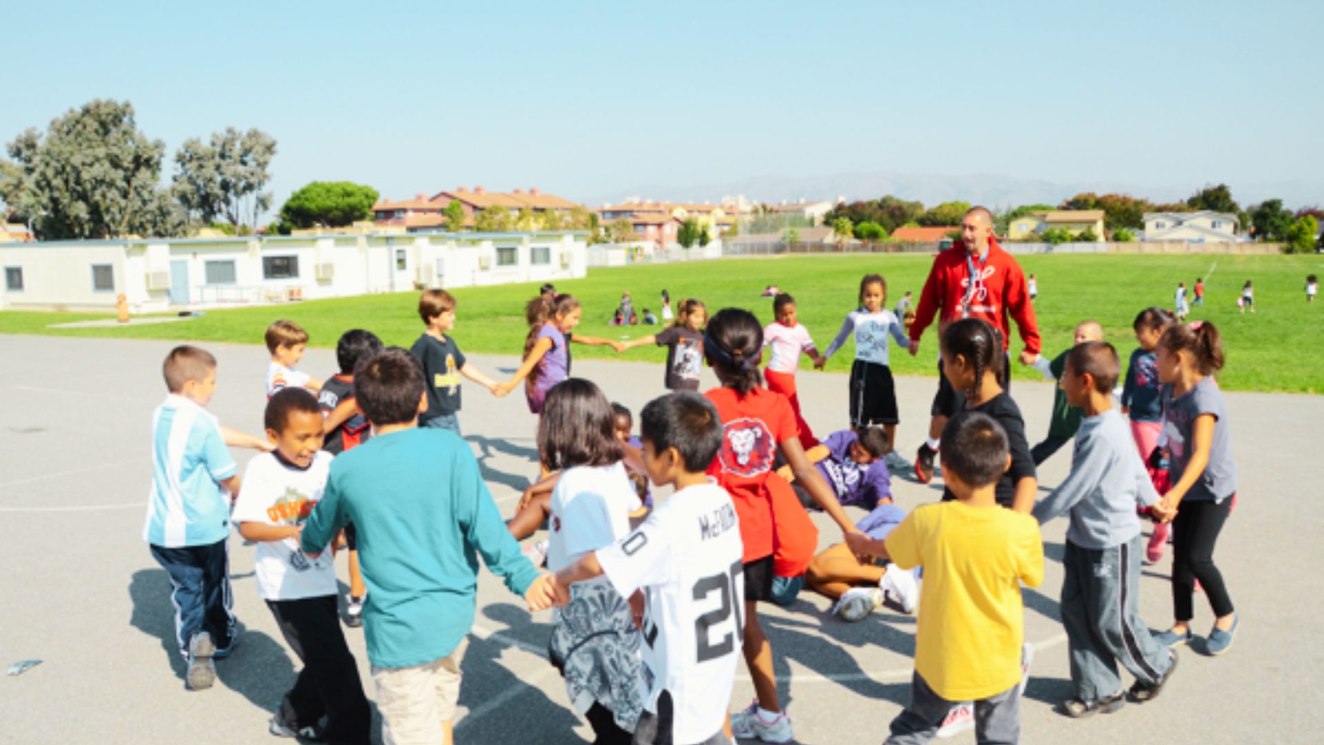 A group of children gathers around a man, engaging in conversation and sharing smiles in a lively outdoor setting.