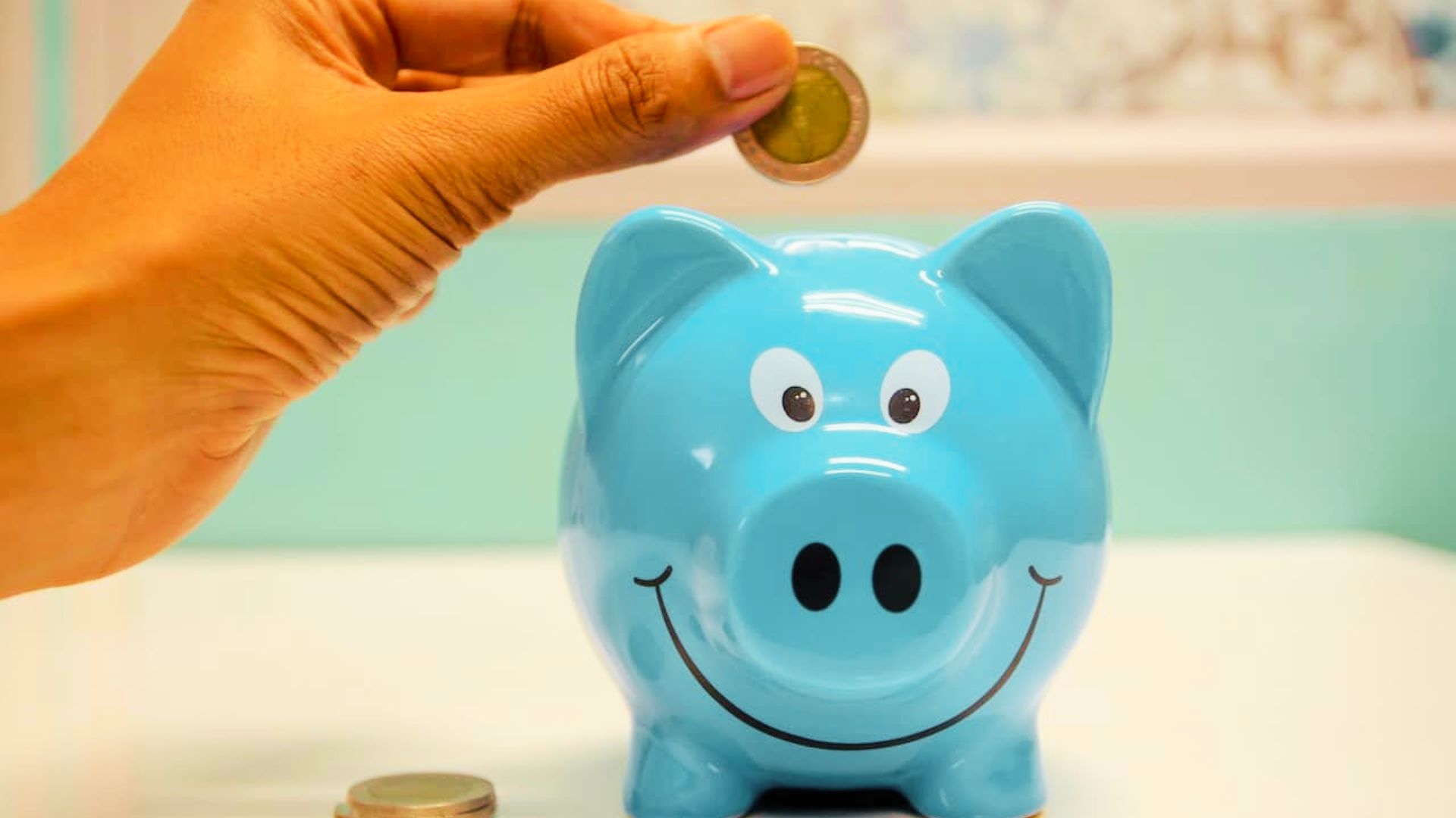 A person inserting a coin into a piggy bank, symbolizing saving and financial responsibility for teens.