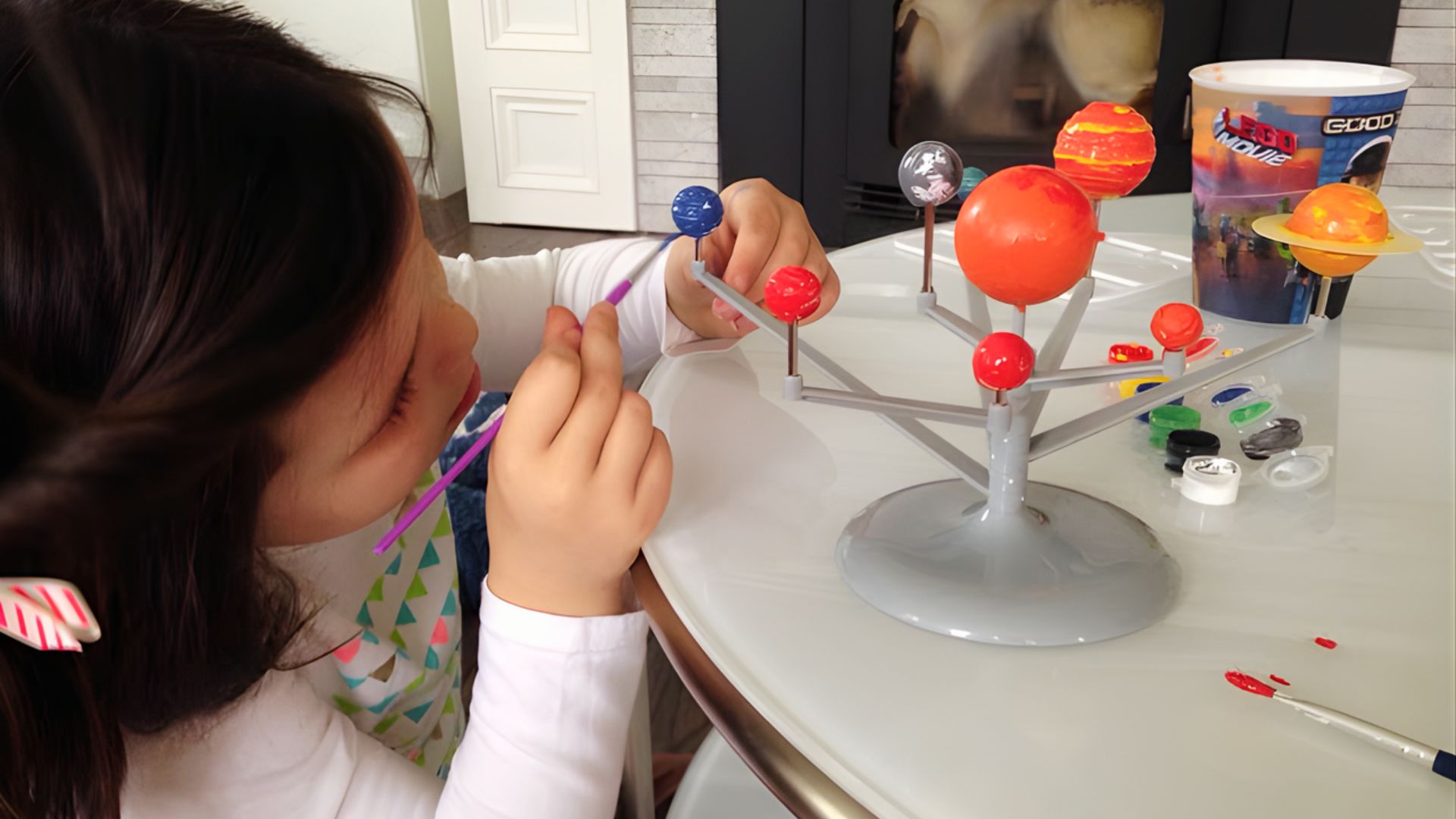 A young girl is engaged in painting a detailed model of the solar system as part of a creative learning activity.