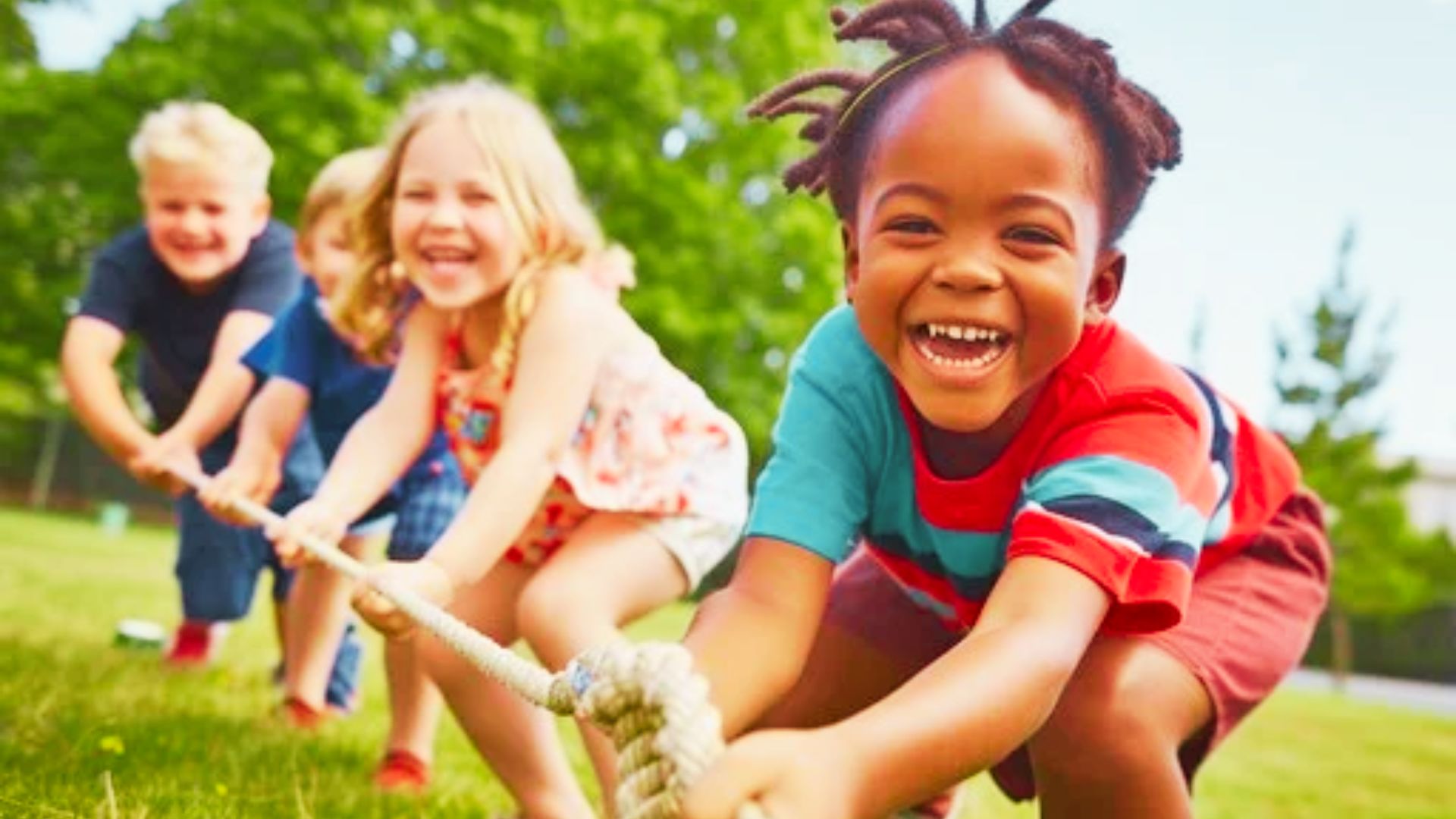 Children engaged in a tug of war on a grassy field, smiling and pulling a rope together in a playful competition.