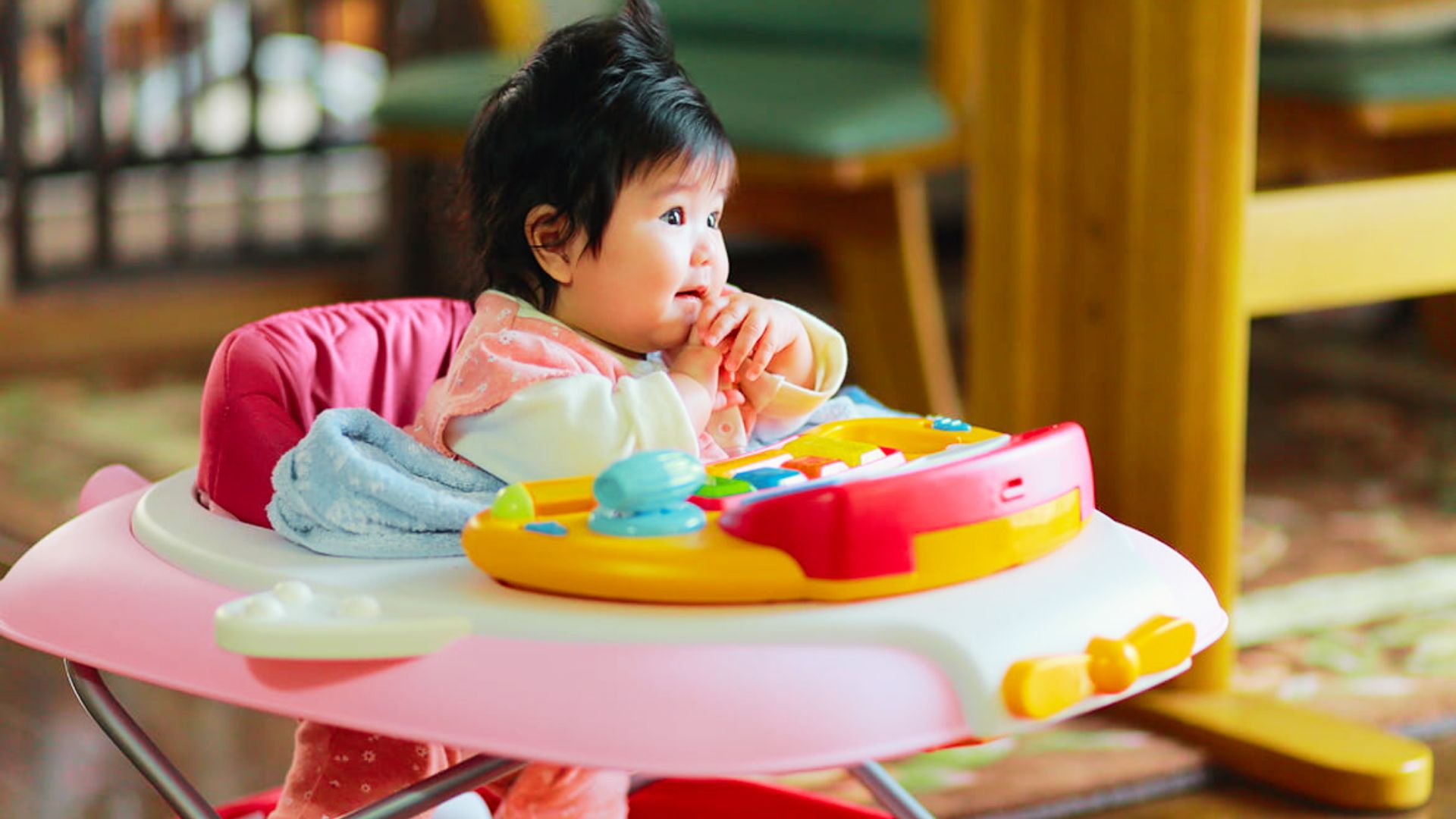 A baby sitting in a pink baby walker, smiling and exploring their surroundings.