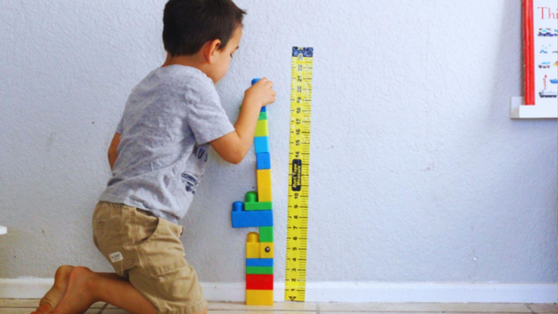 A young boy is engaged in play, constructing with a colorful Lego ruler on a table.