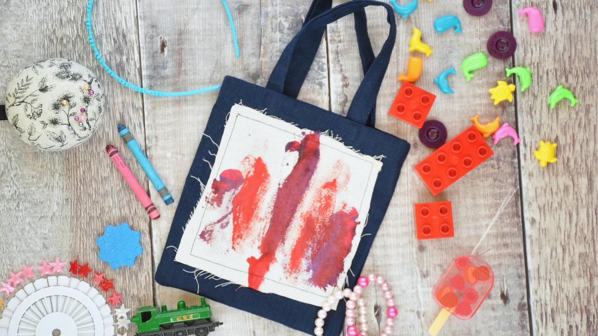 Navy tote bag with painted patch, crayons, beads, LEGO bricks, toy train, crafts.